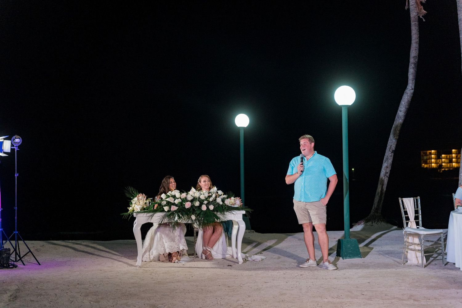 Man gives speech at elegant beach wedding reception table decorated with white florals.