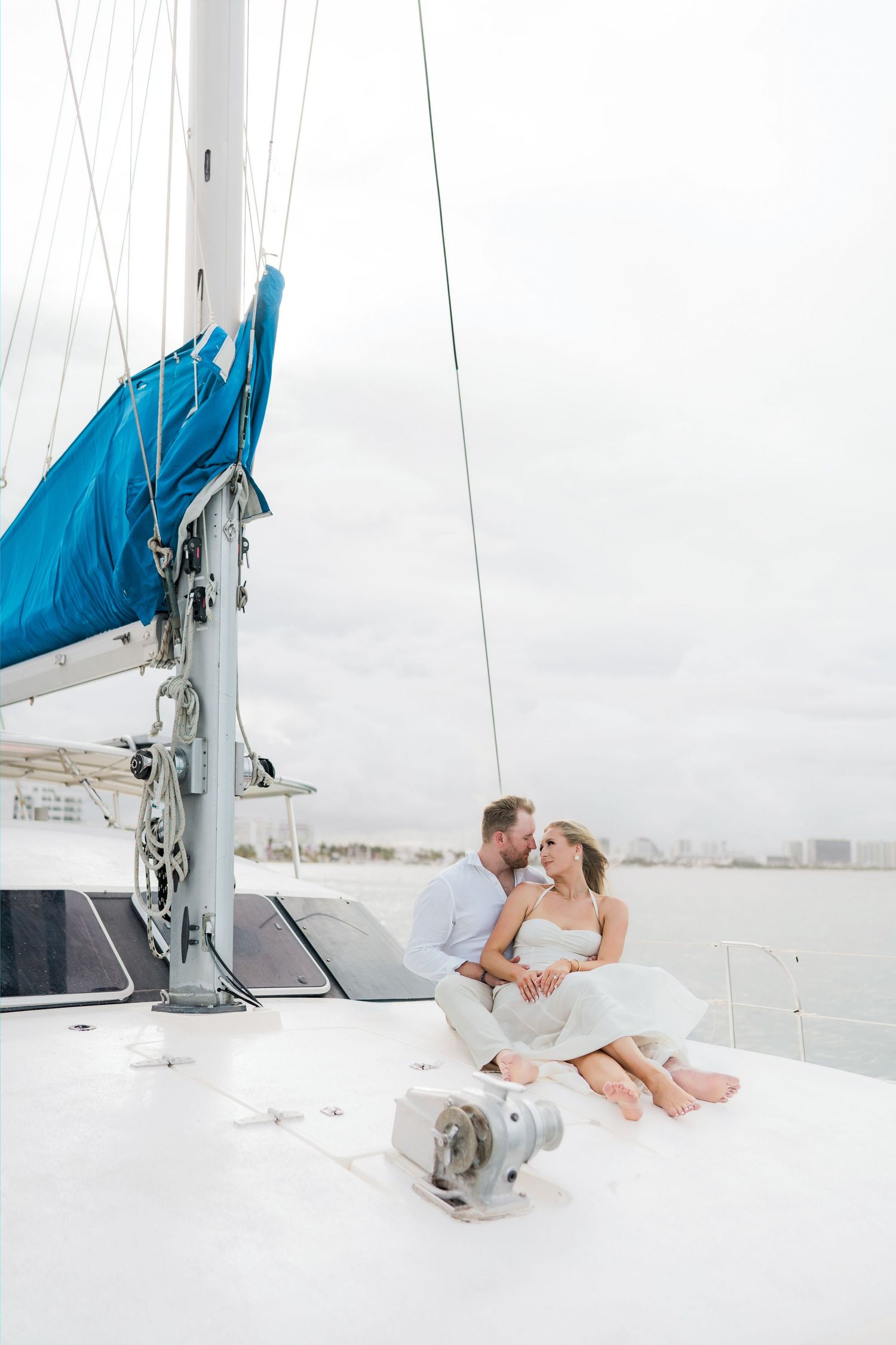 CANCÚN ENGAGEMENT PHOTOSHOOT - Couple sitting closely together on the deck of a white sailboat