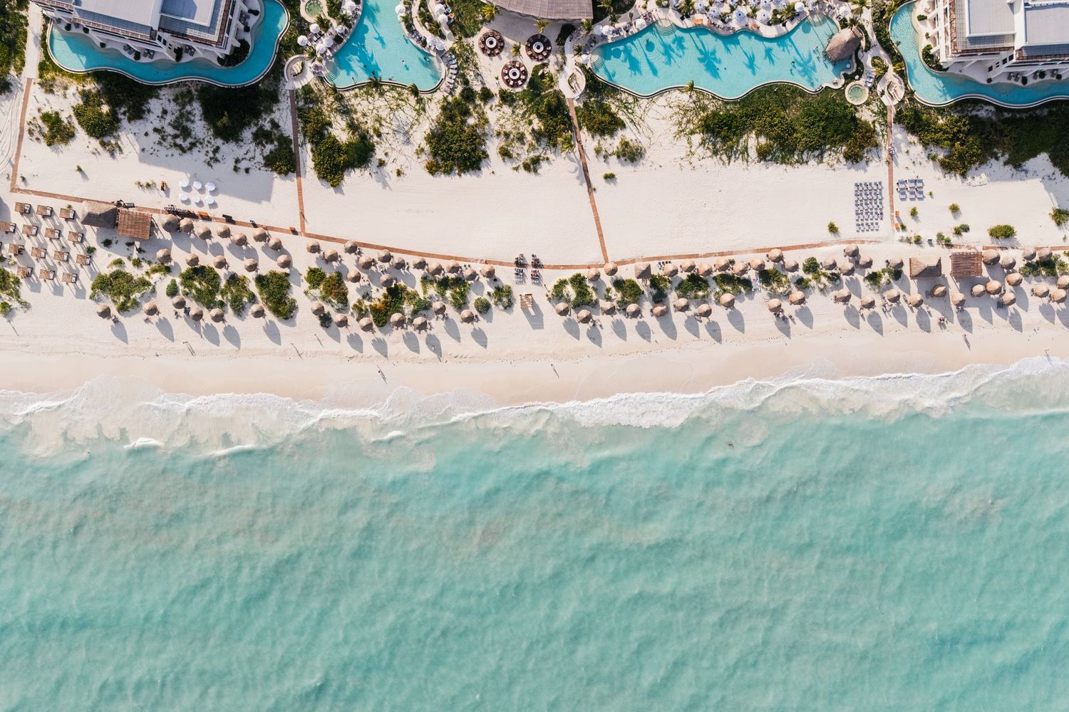Aerial view of a luxury beach resort with turquoise water, white sand, pools, and palm trees in a tropical destination.