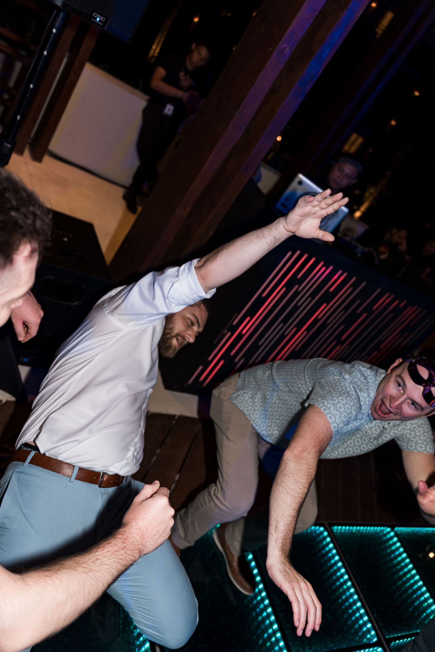 Men dancing energetically on a lit dance floor at a nightclub or party event.