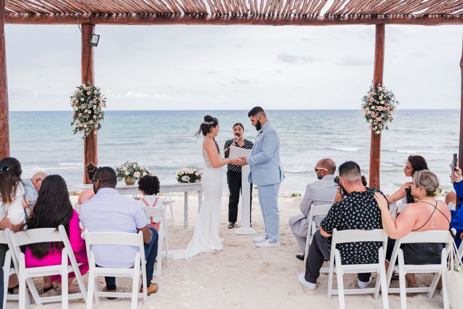 Bride and groom stand at altar during intimate beach wedding ceremony with small group of seated guests.