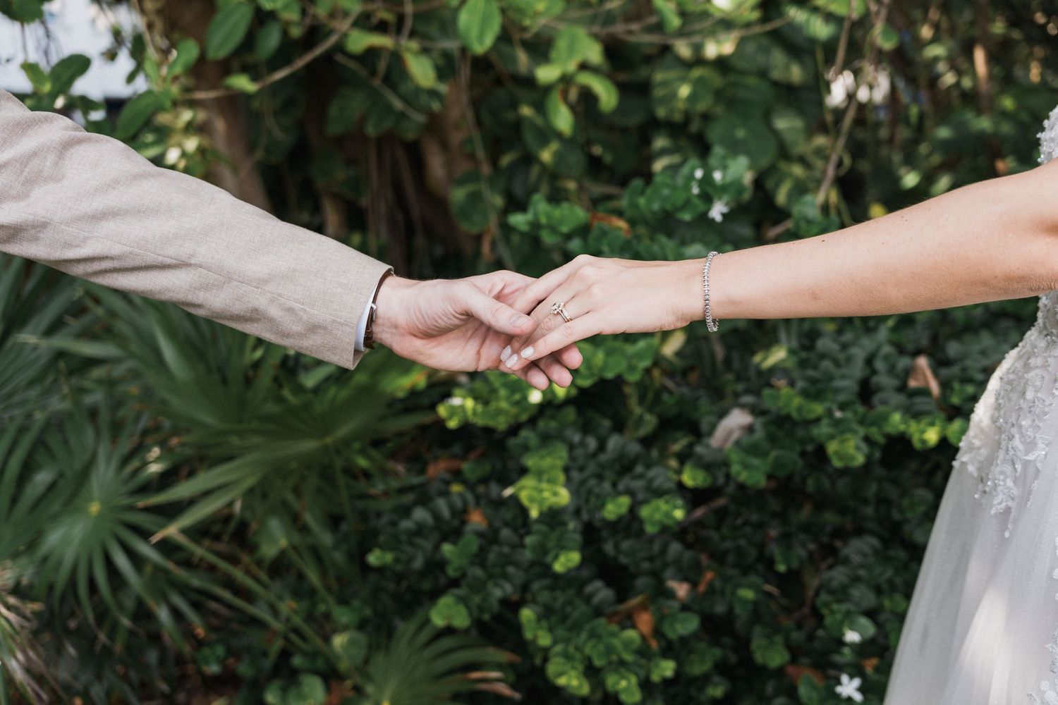 Bride and groom holding hands outdoors with lush tropical greenery in the background at their wedding.
