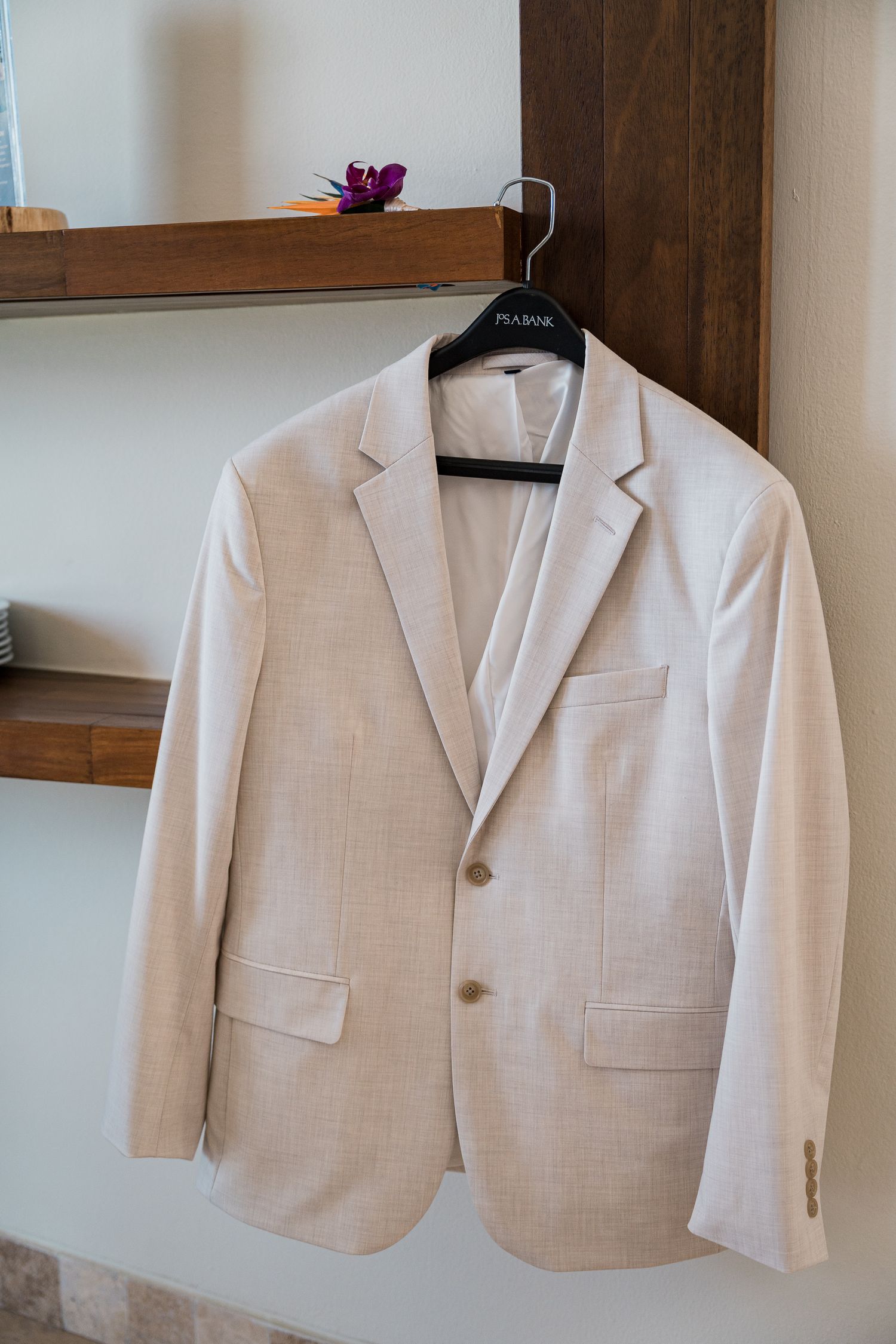 Hotel Xcaret México Wedding  - Elegant cream blazer on a hanger, displayed against a white wall with wooden shelves in the background.