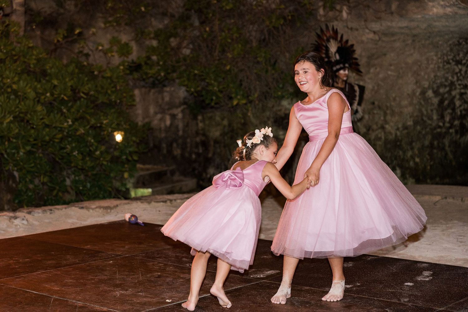 Two girls in matching pink tulle dresses dance together at a formal event, one holding sparklers.