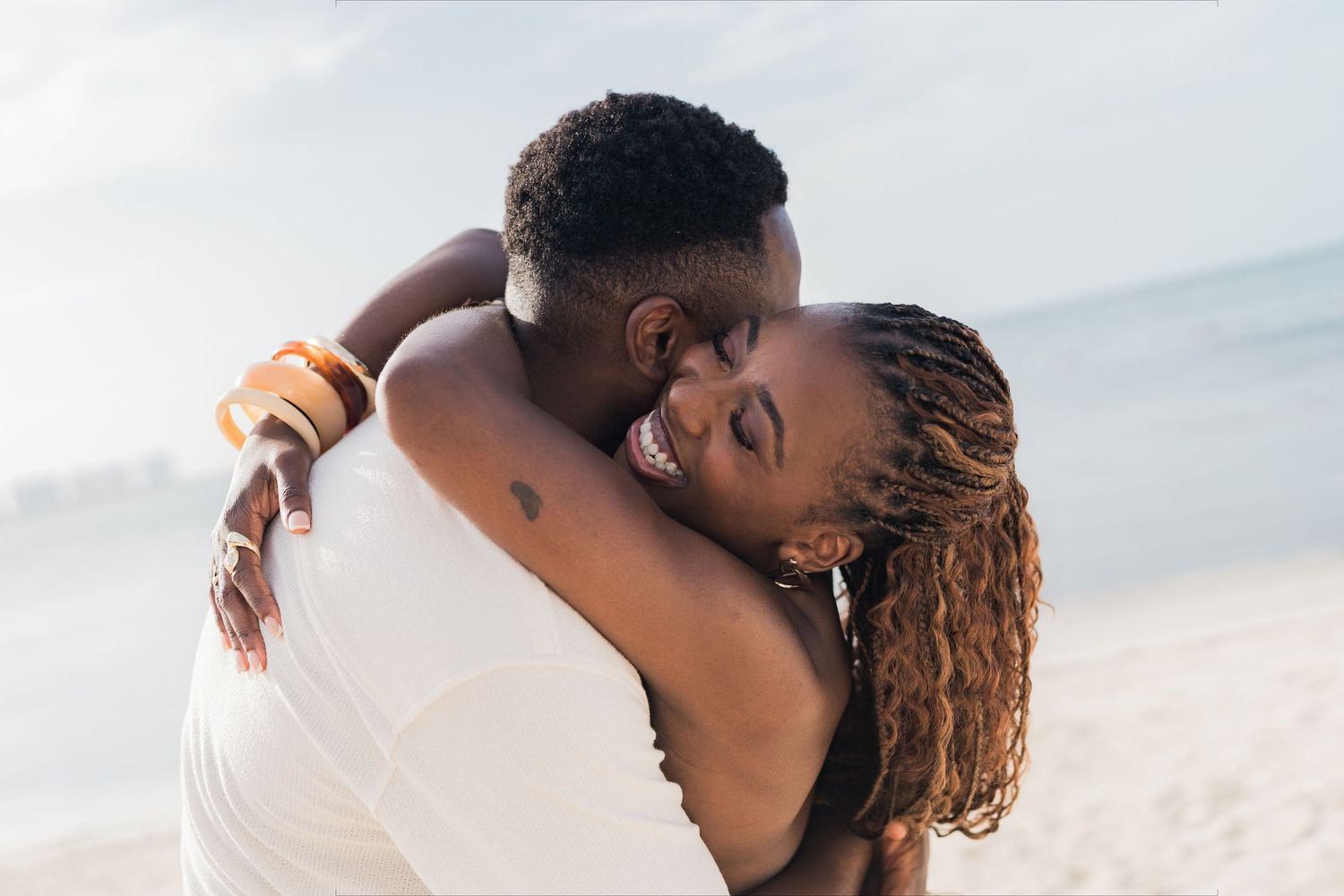 A joyful couple embracing on a sunny beach, sharing a tender moment with warm smiles.