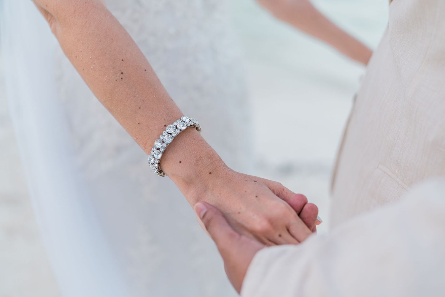 Close-up of bride wearing diamond tennis bracelet holding hands on beach.