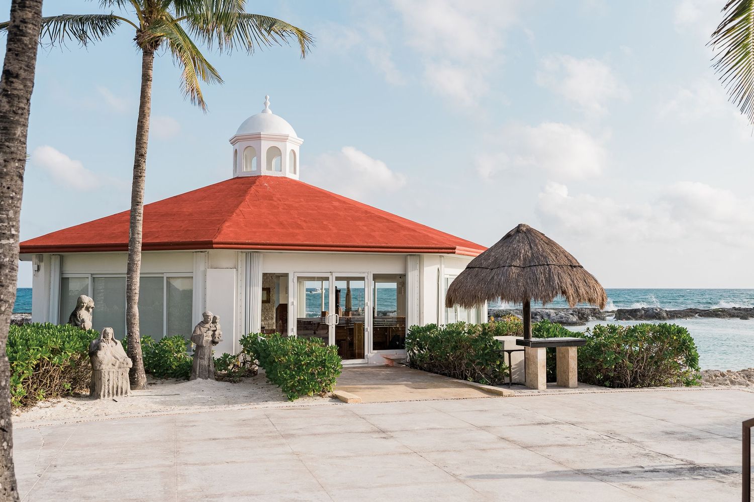 Elegant beachside wedding venue chapel with red roof and palapa near the crystal blue ocean.