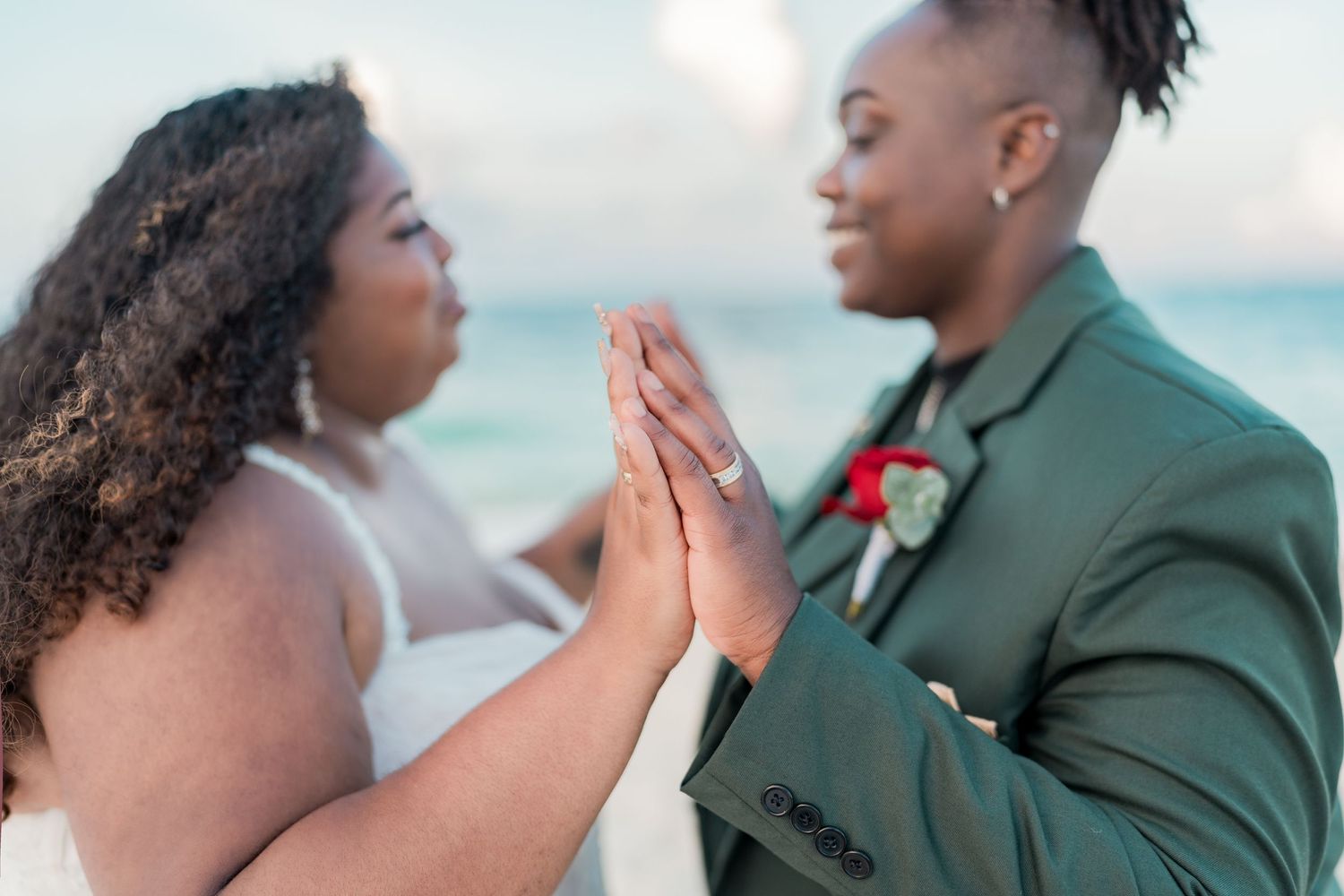 Lesbian couple in wedding attire hold hands and gaze at each other on a beautiful Caribbean beach.