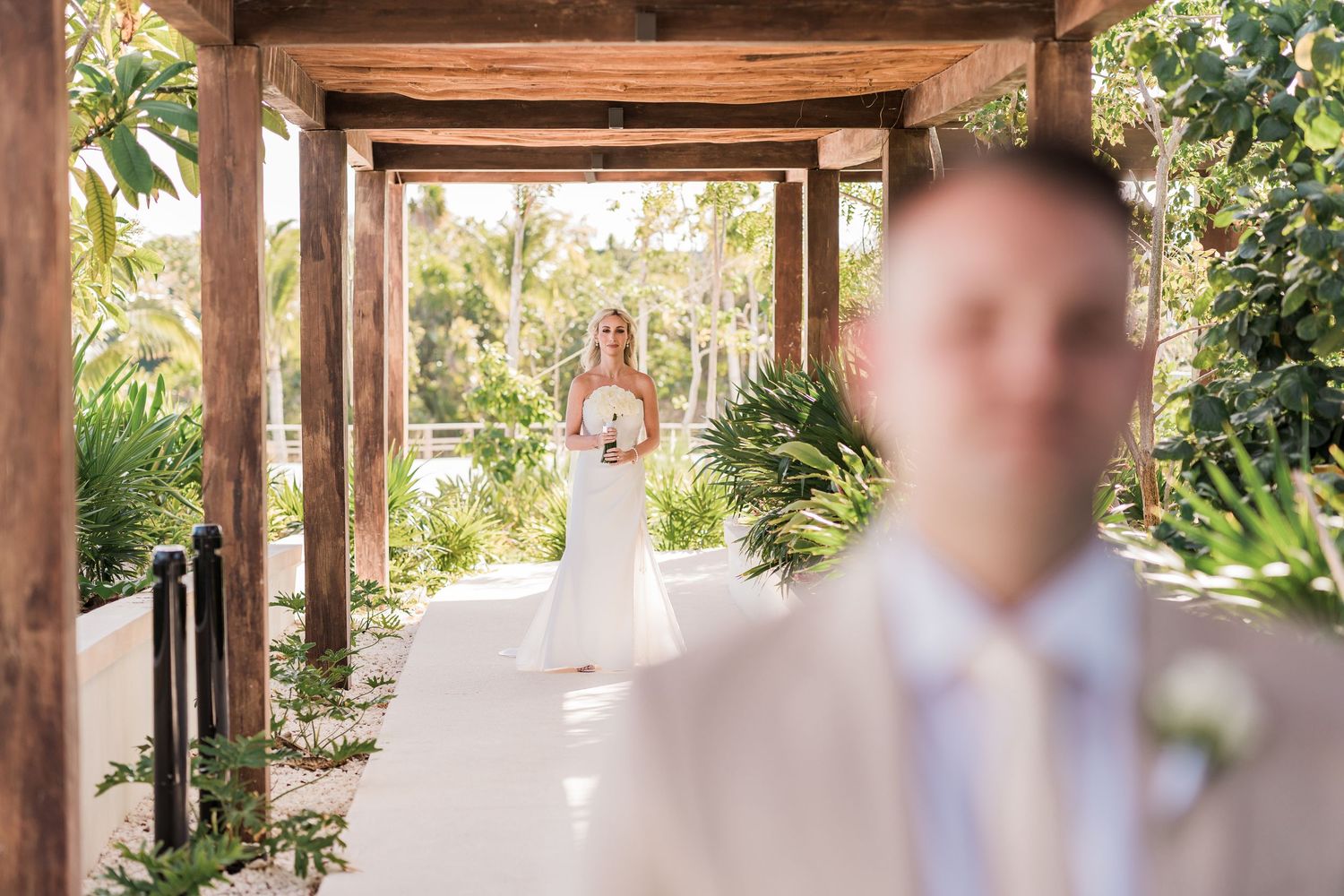 Bride in white gown walks toward groom during first look at tropical resort wedding venue.