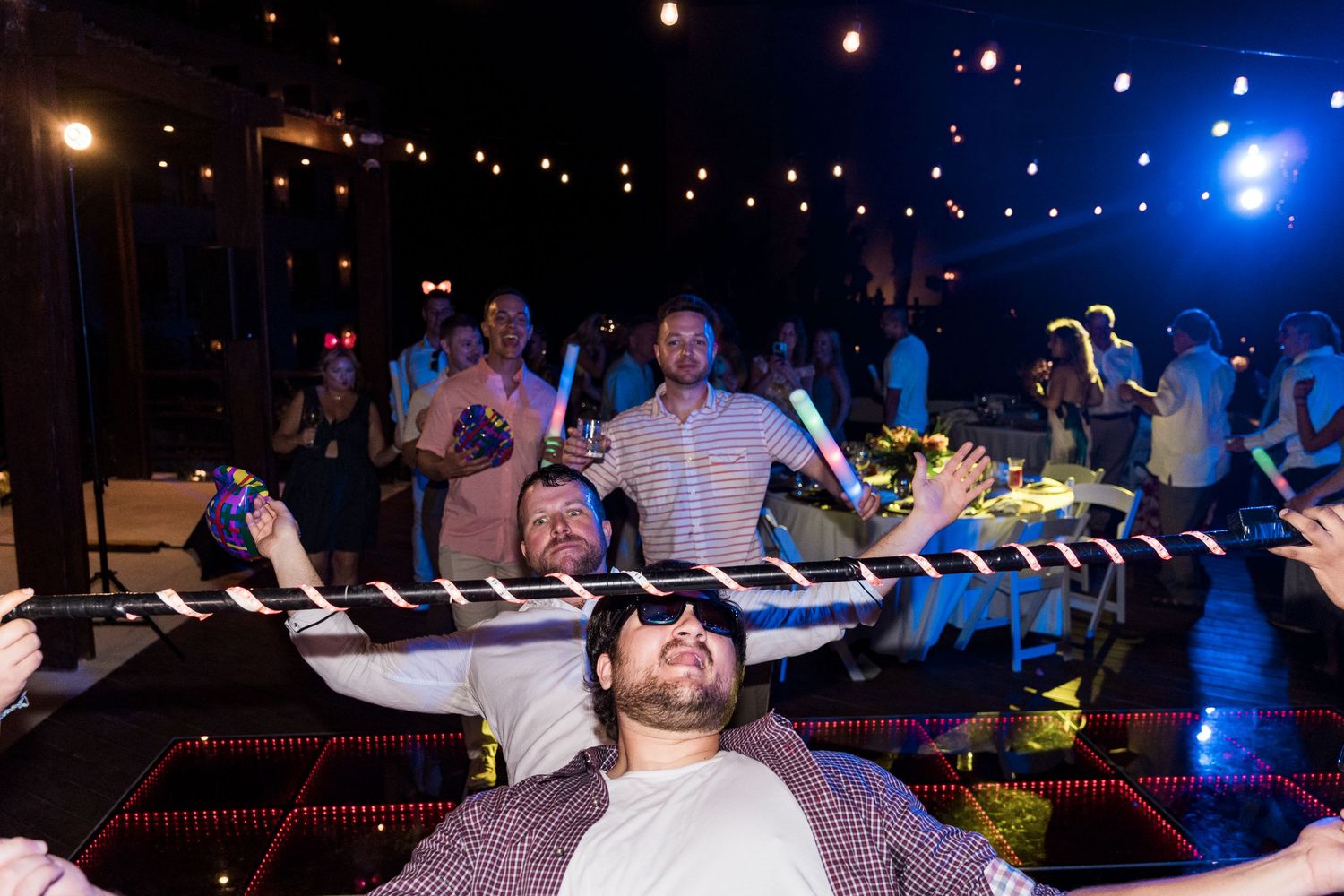 Guests dancing and celebrating at an indoor party with colorful LED lights and glow sticks.