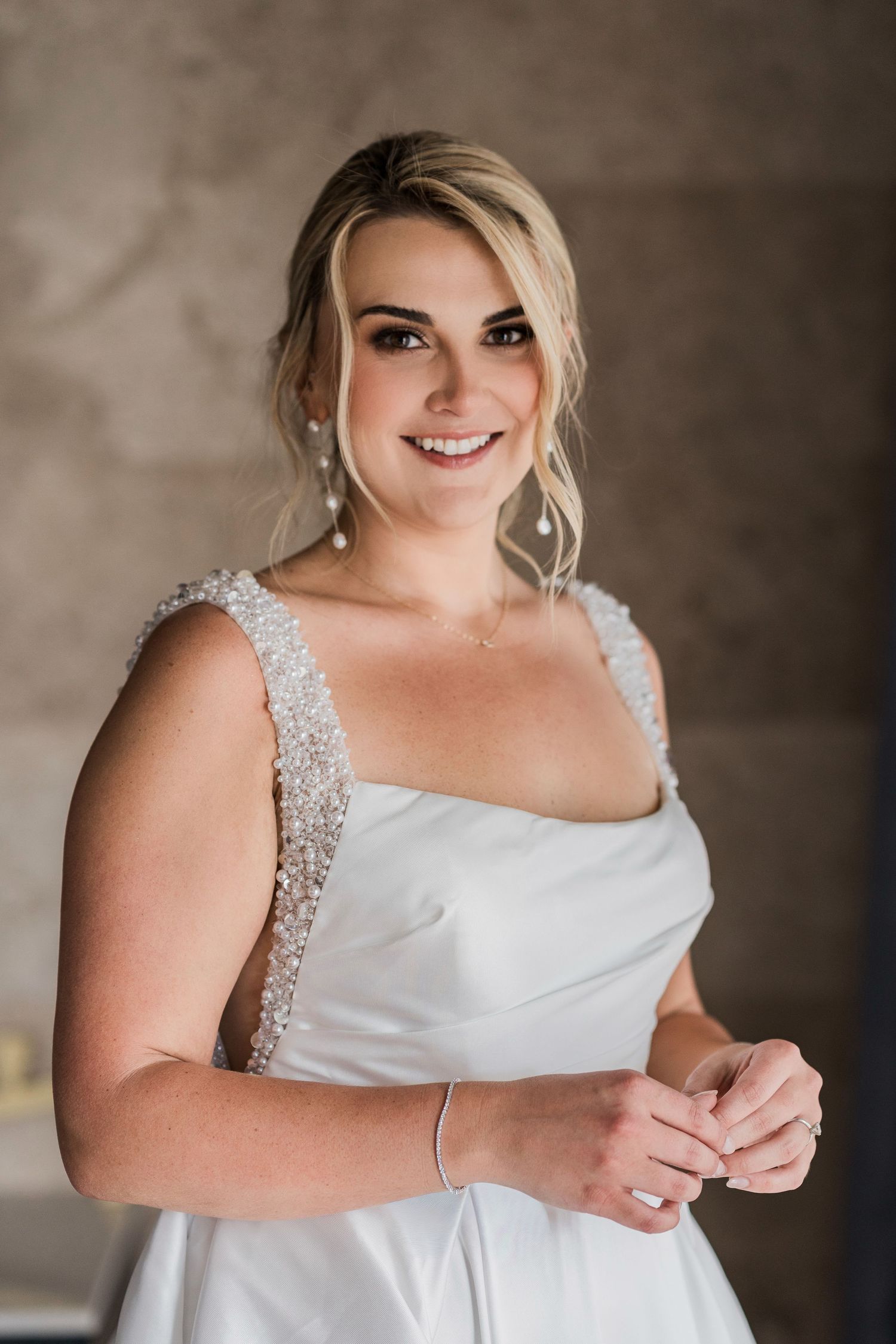 Smiling bride in white beaded gown with updo hairstyle and drop earrings, posing elegantly indoors. Hard Rock Riviera Maya wedding