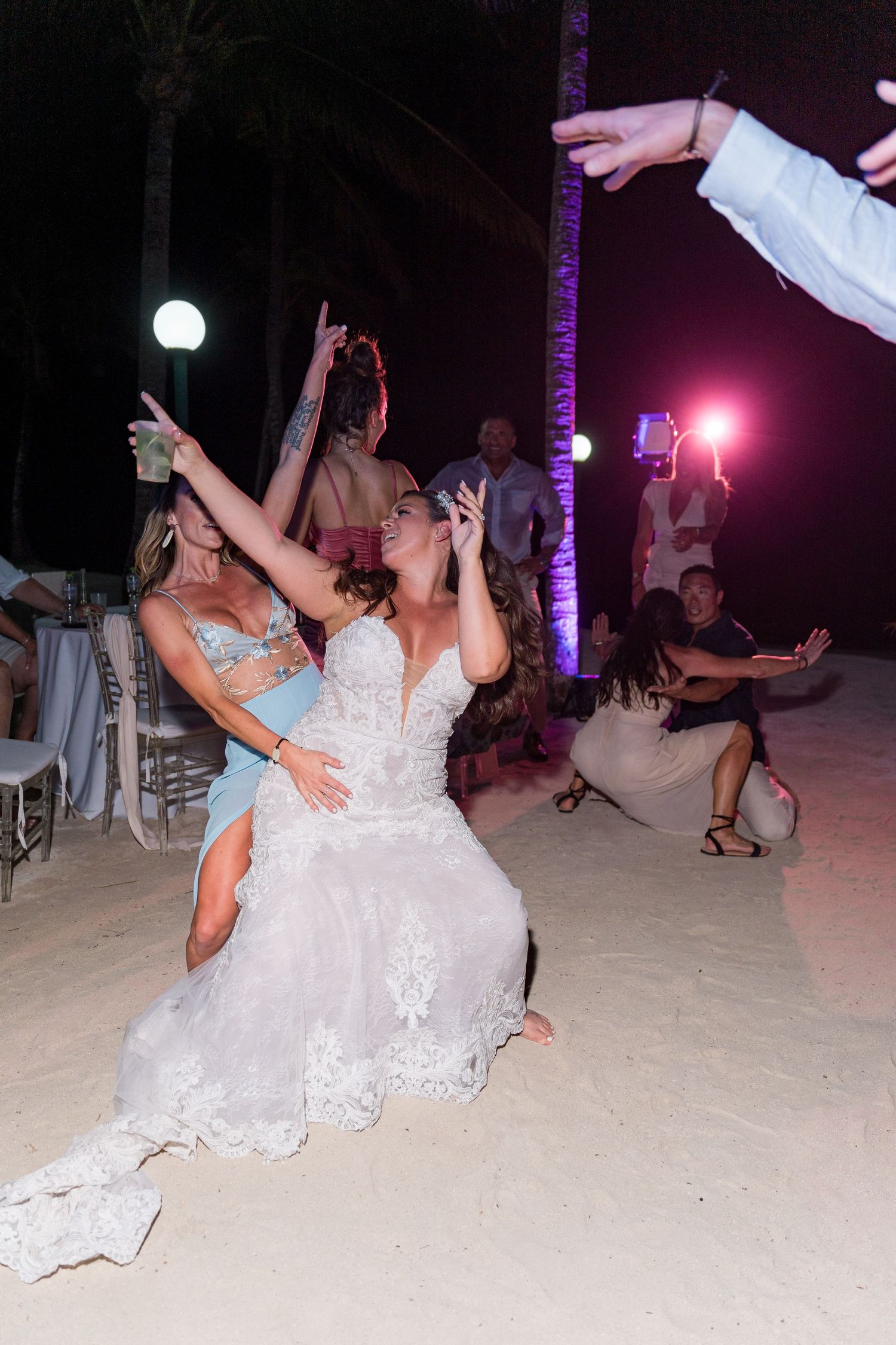 Bride in white lace gown dancing on beach sand at nighttime wedding reception.