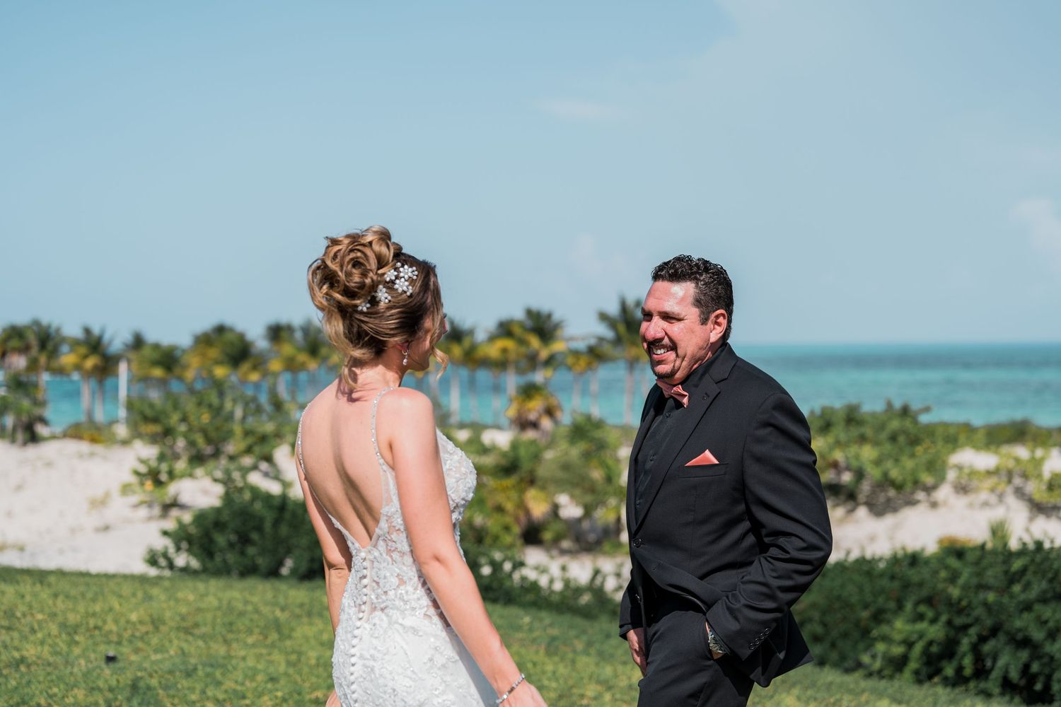 Groom smiling joyfully at bride during first look near tropical beach.
