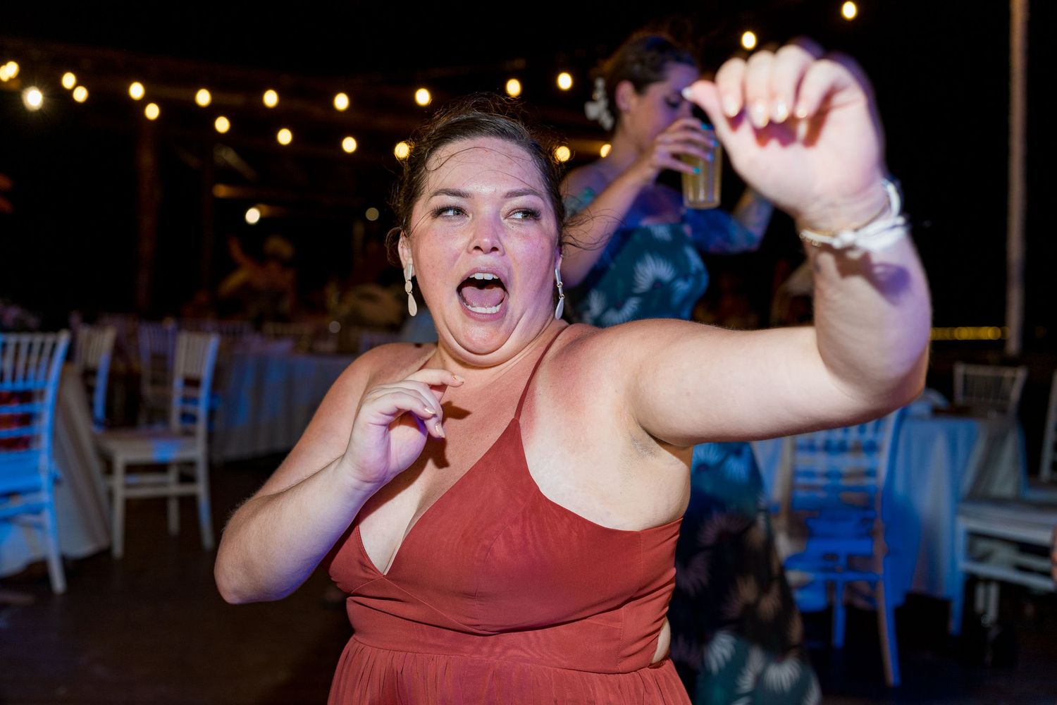 Woman in red dress dancing energetically at outdoor wedding reception under string lights.