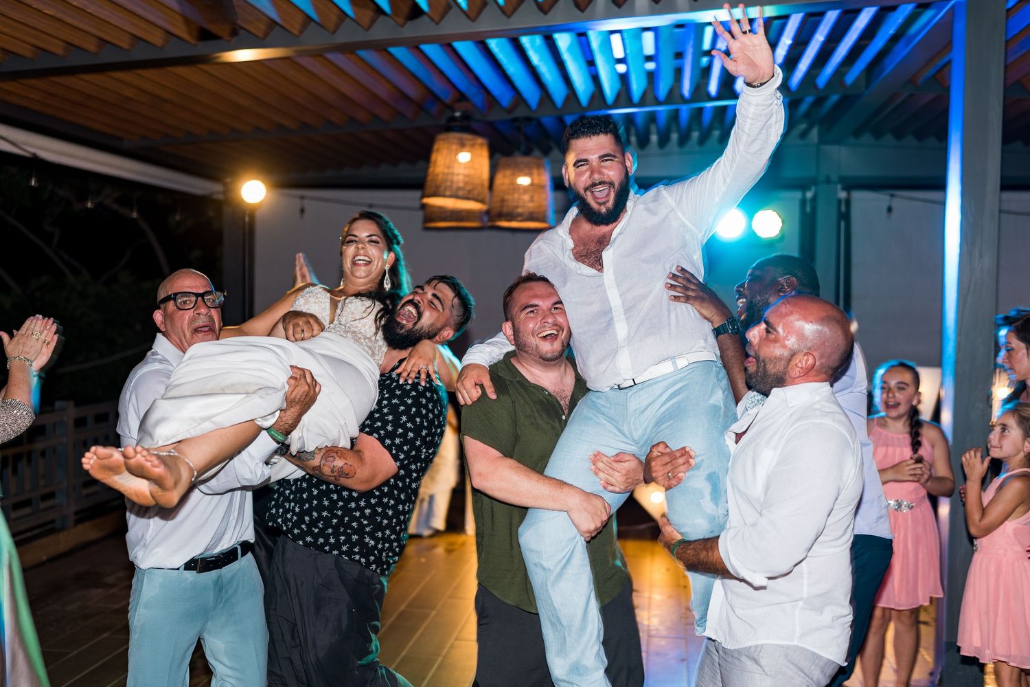 Groom lifted by groomsmen on wedding dance floor with guests celebrating in background.