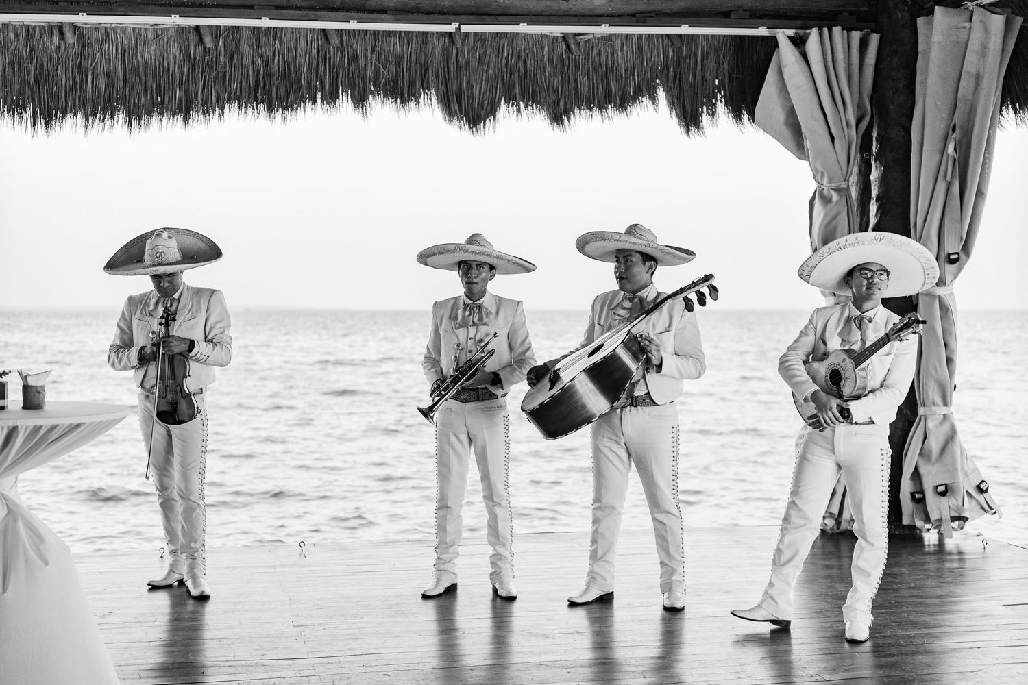 Mariachi band in traditional charro suits performing by the ocean at a beach wedding reception.