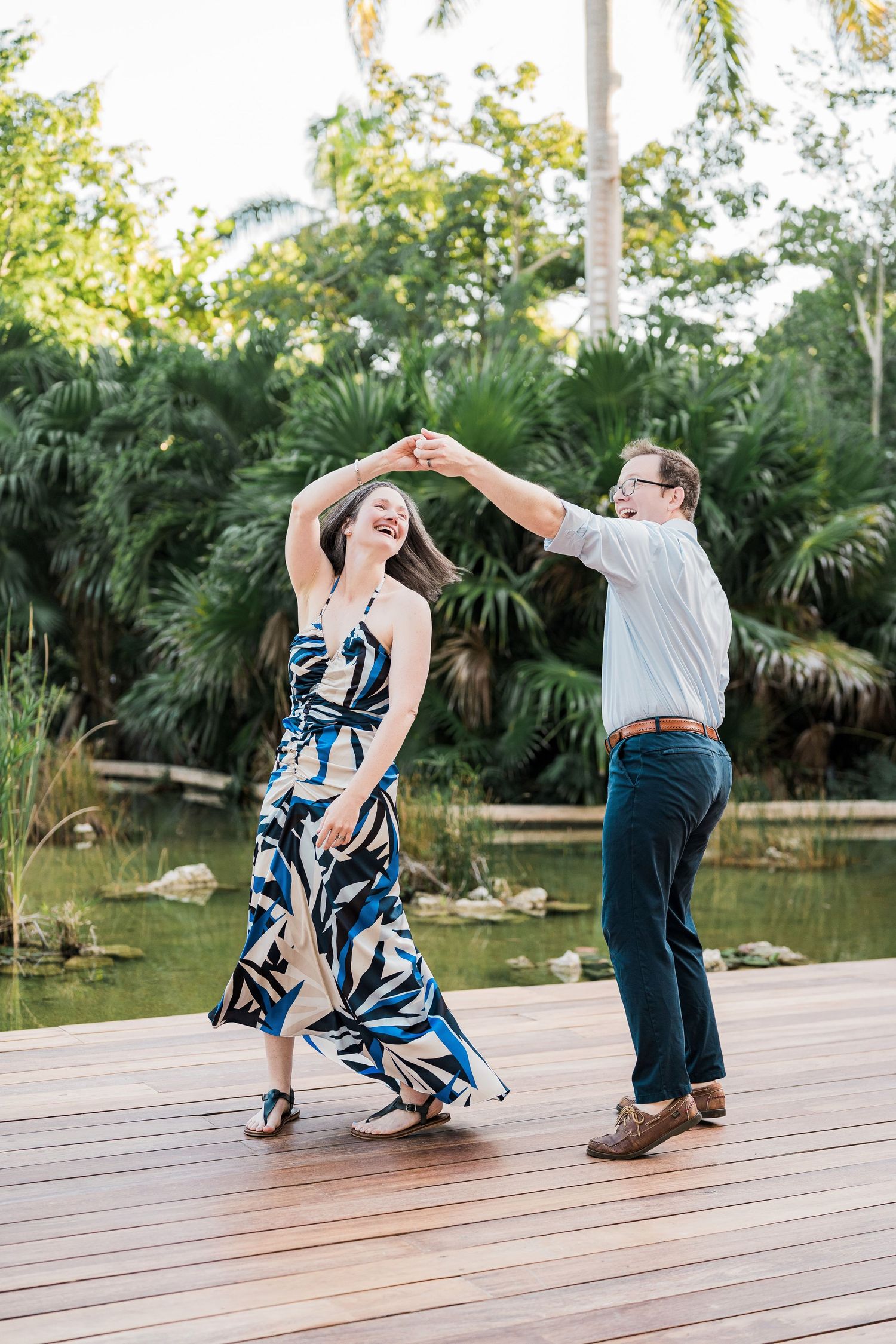 Secrets Akumal Wedding - Couple dancing joyfully on a wooden deck surrounded by tropical greenery near a pond.