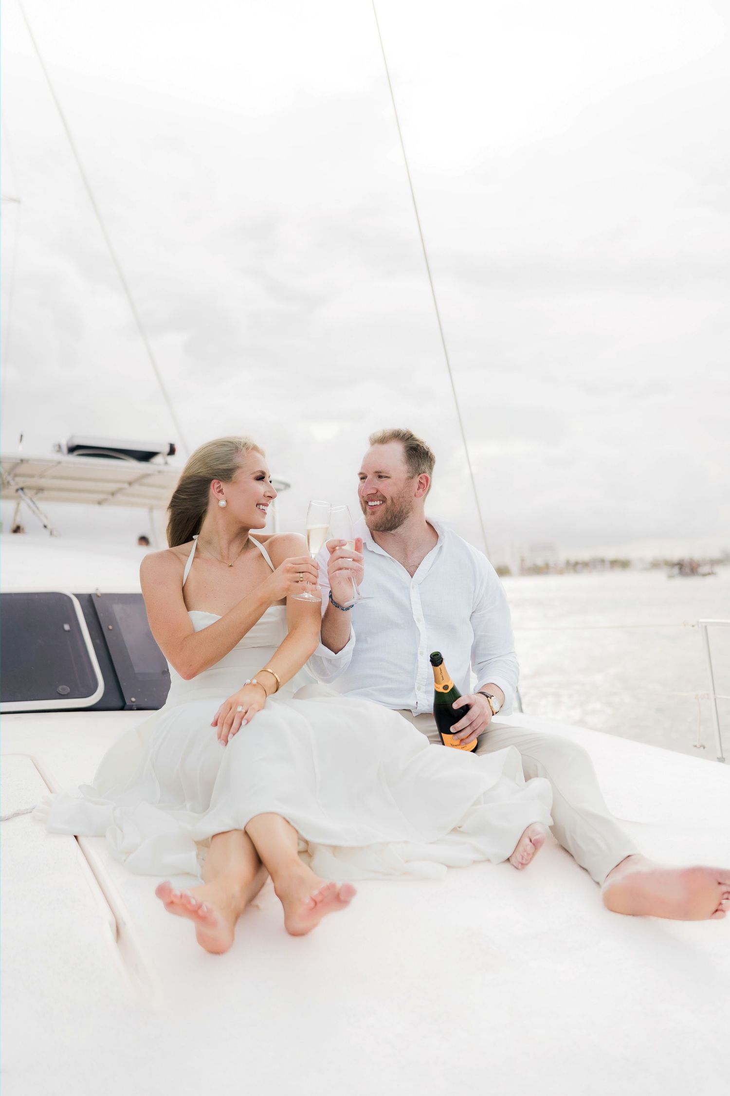Cancun Engagement Photoshoot - Happy couple toasting champagne glasses on a sailboat deck, smiling and celebrating together.