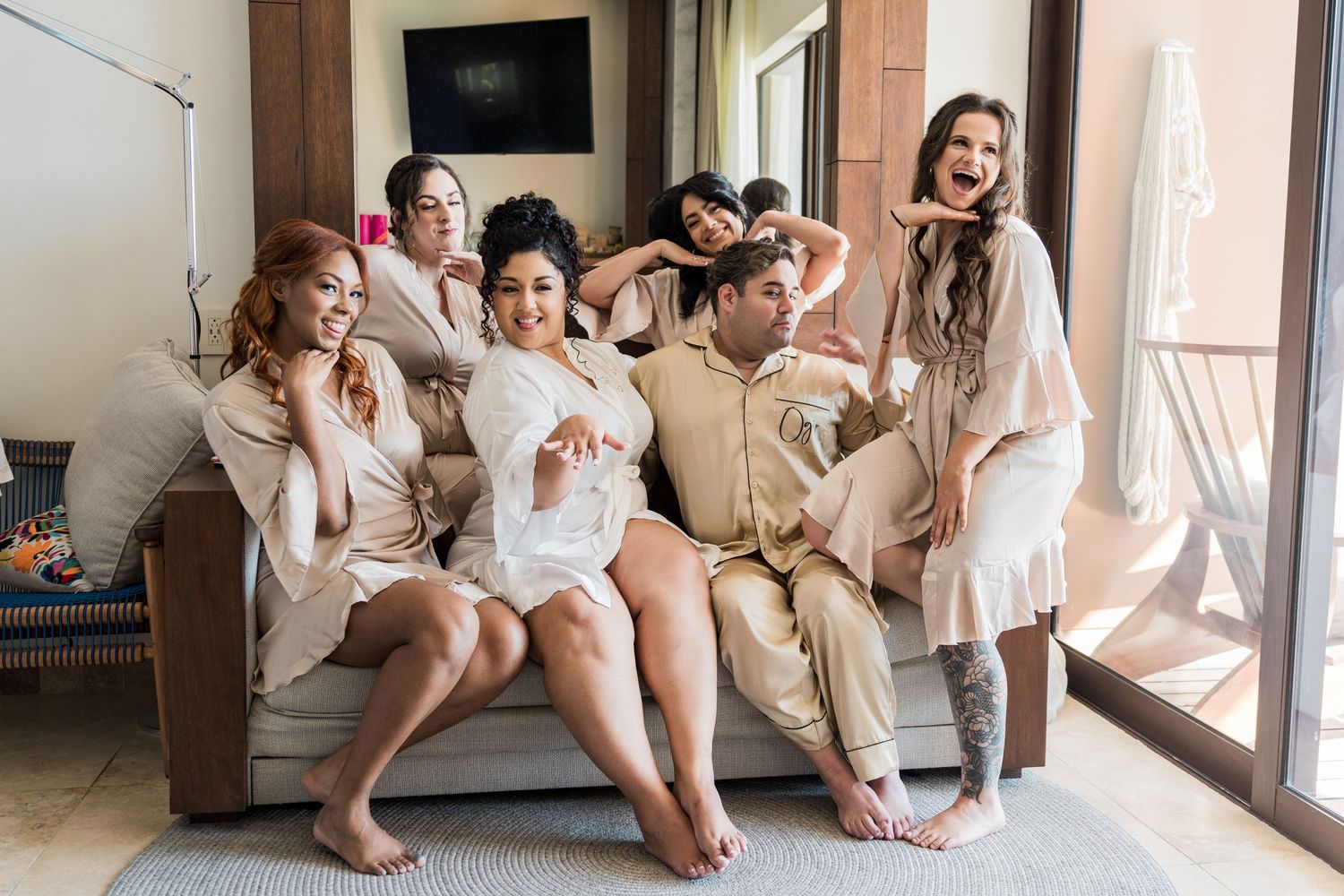 Xcaret Arte Wedding - Bridal party in matching robes laughing and posing together on a couch during wedding morning preparations.