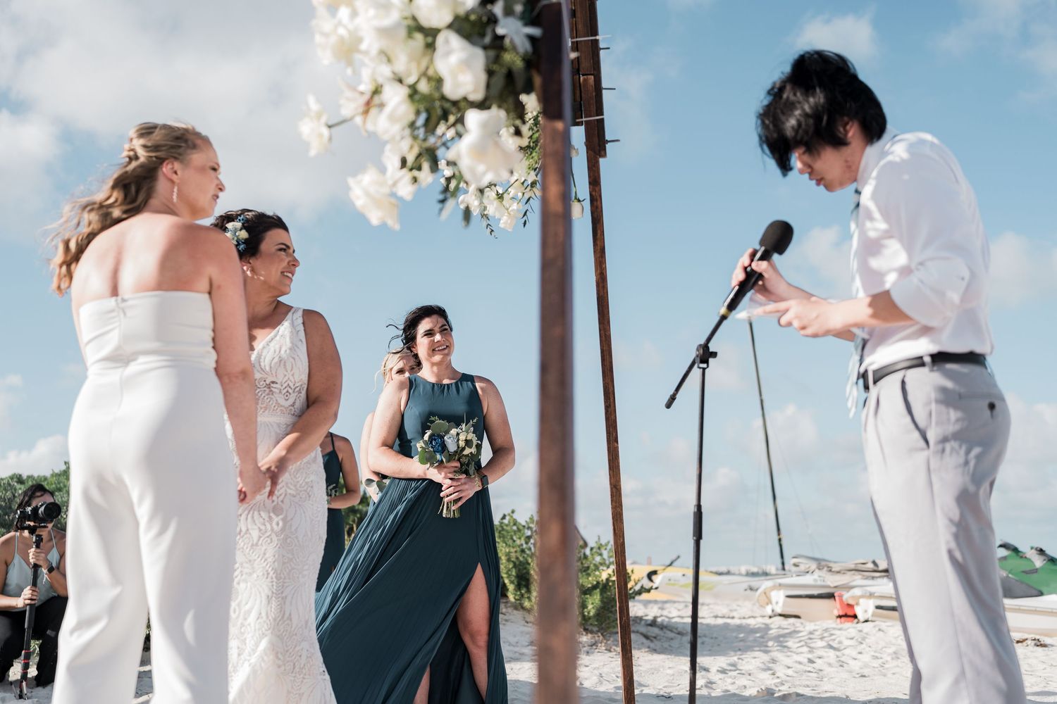 Officiant reads vows at beach wedding ceremony with bride, groom, and bridesmaid standing nearby.