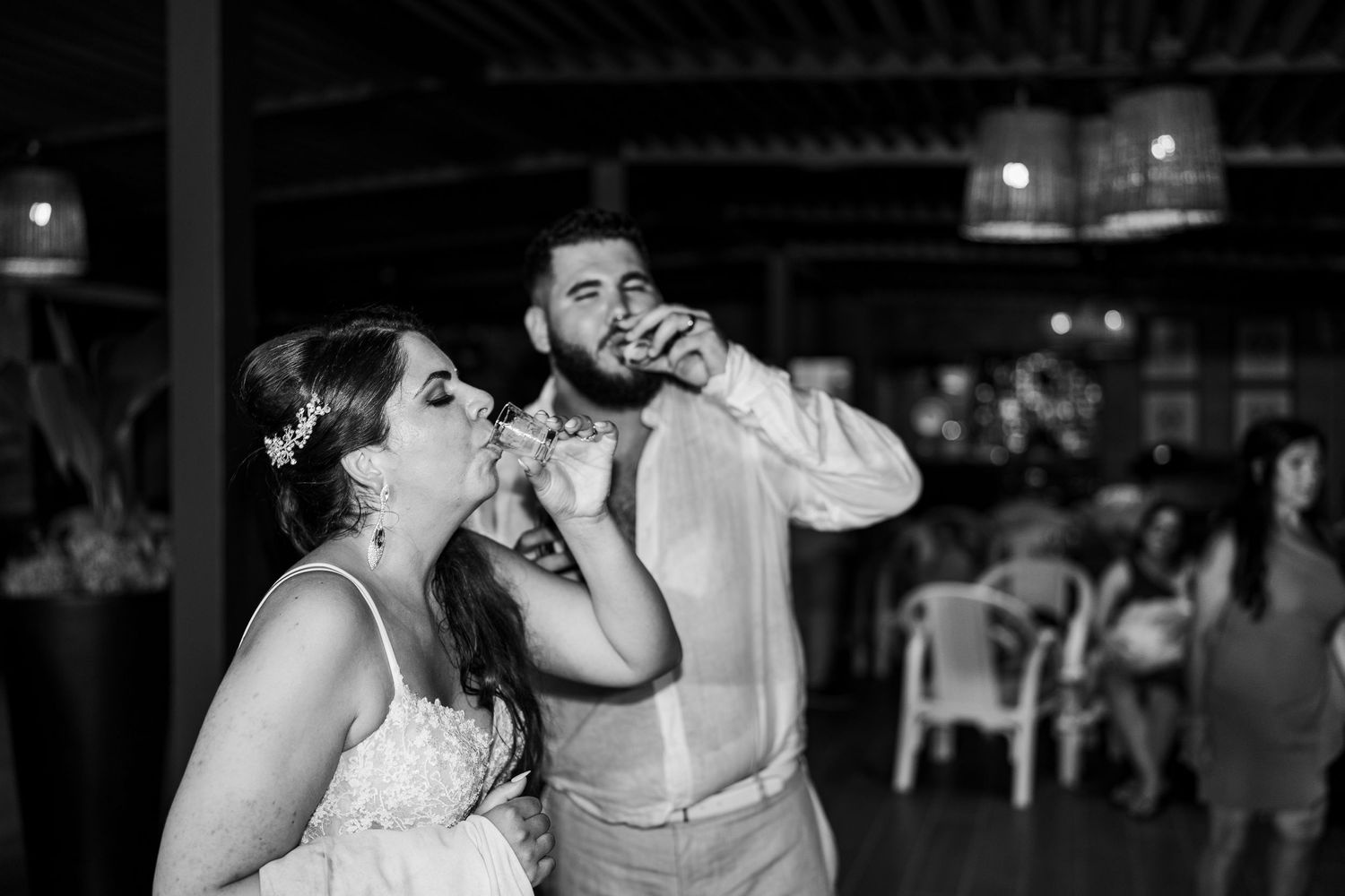 Bride and groom share a playful moment drinking together at their wedding reception in black and white.