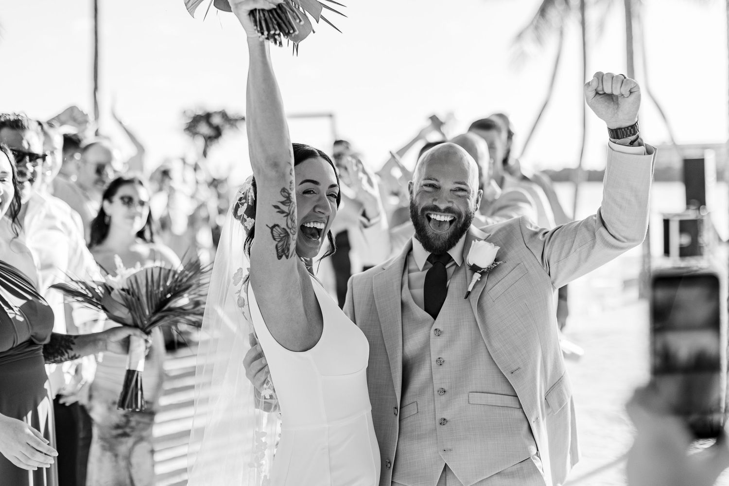 Black and white photo of joyful newlyweds celebrating after wedding ceremony on tropical beach.