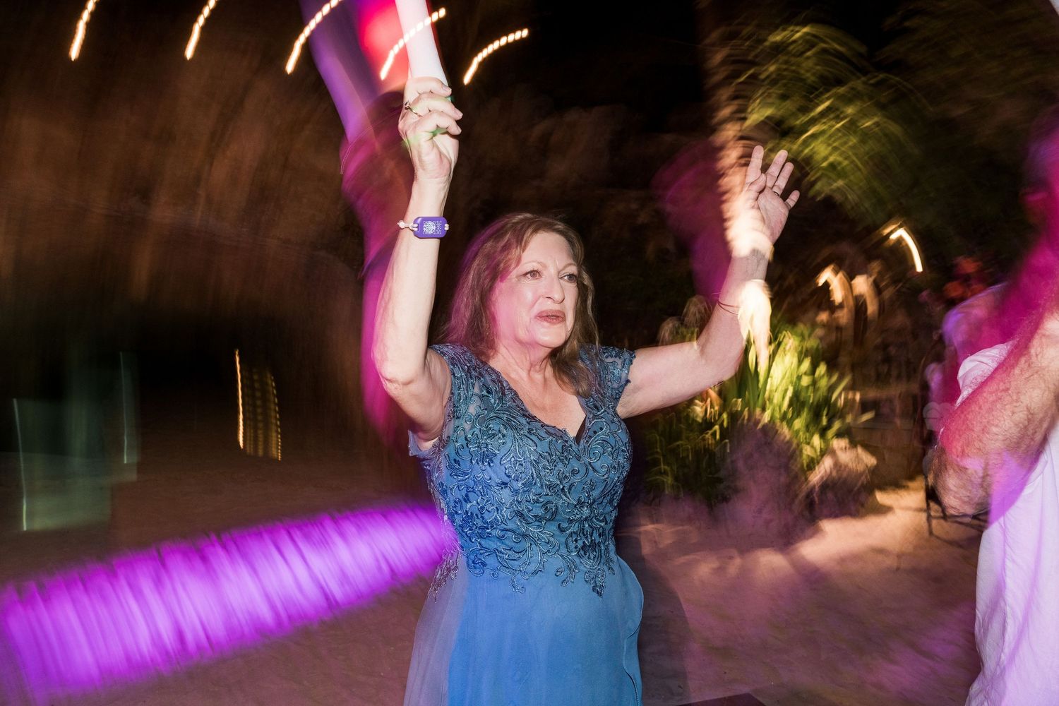 Woman in blue dress dancing joyfully with arms raised at an outdoor evening party with colorful lights.