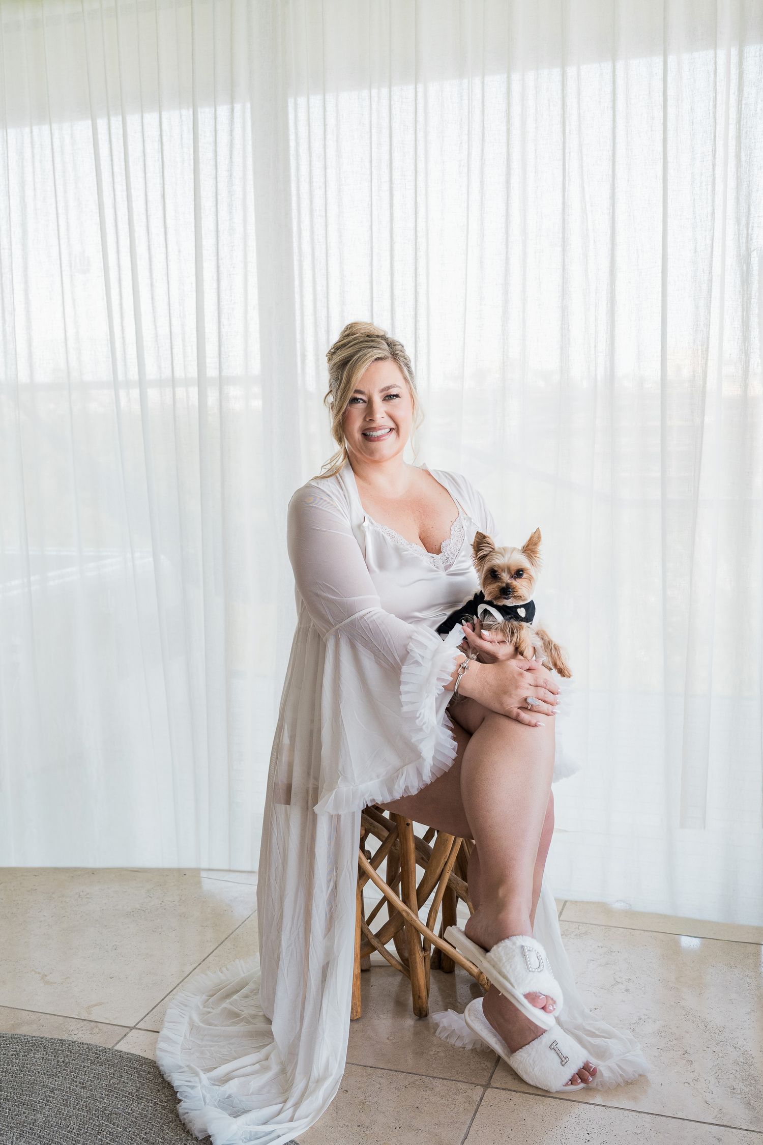 Hotel Xcaret México Wedding  - Smiling bride in white robe holding small Yorkshire Terrier dog while seated.