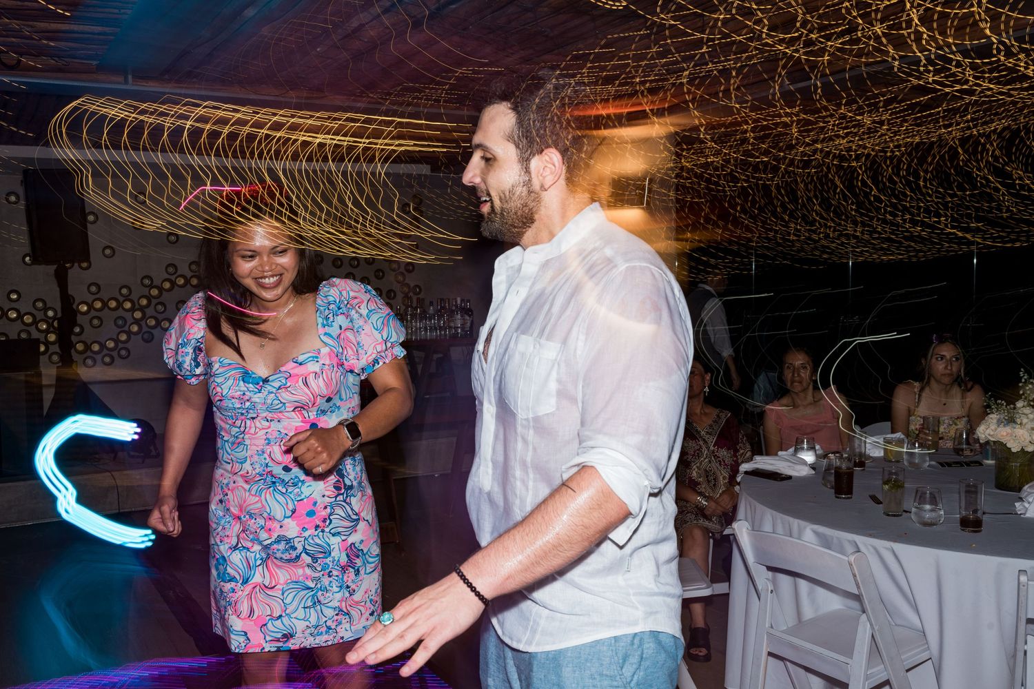 Couple dancing together under colorful lights at a lively outdoor wedding reception at night.