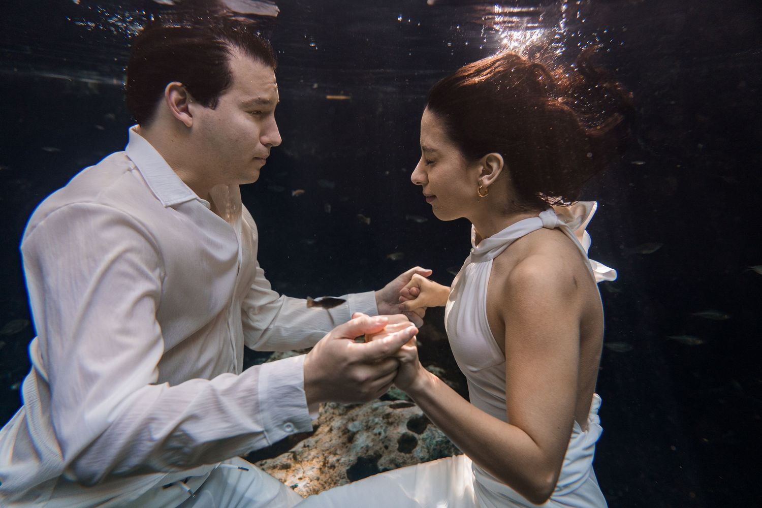 Couple in white attire holding hands in an enchanting underwater photo shoot.