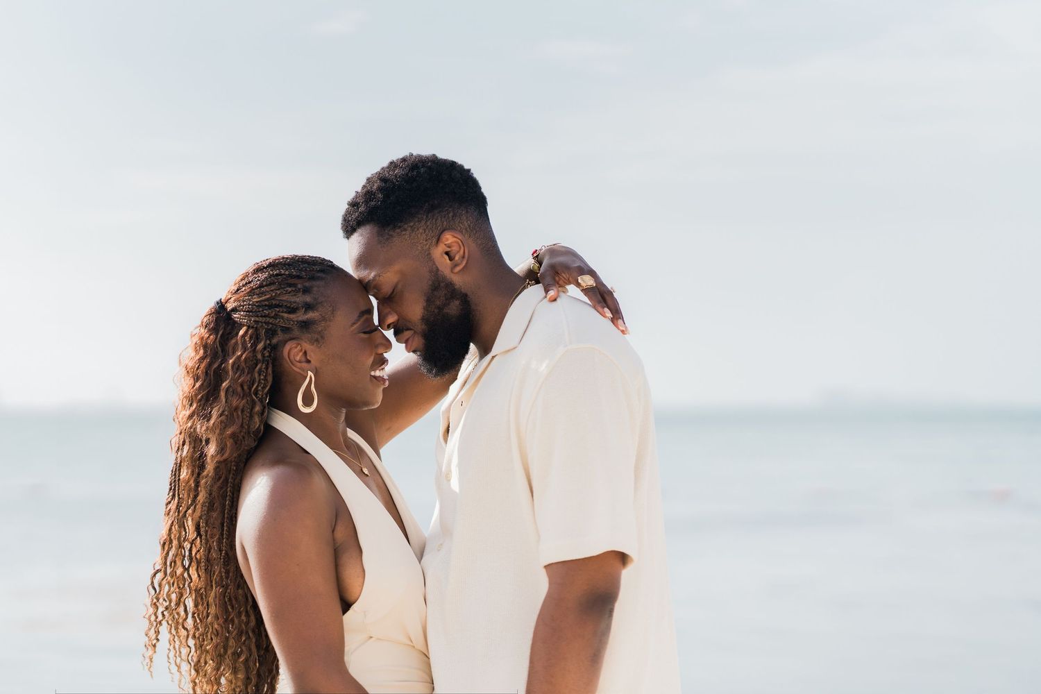 A romantic couple sharing an intimate moment on a beach, touching foreheads with the ocean in the background.