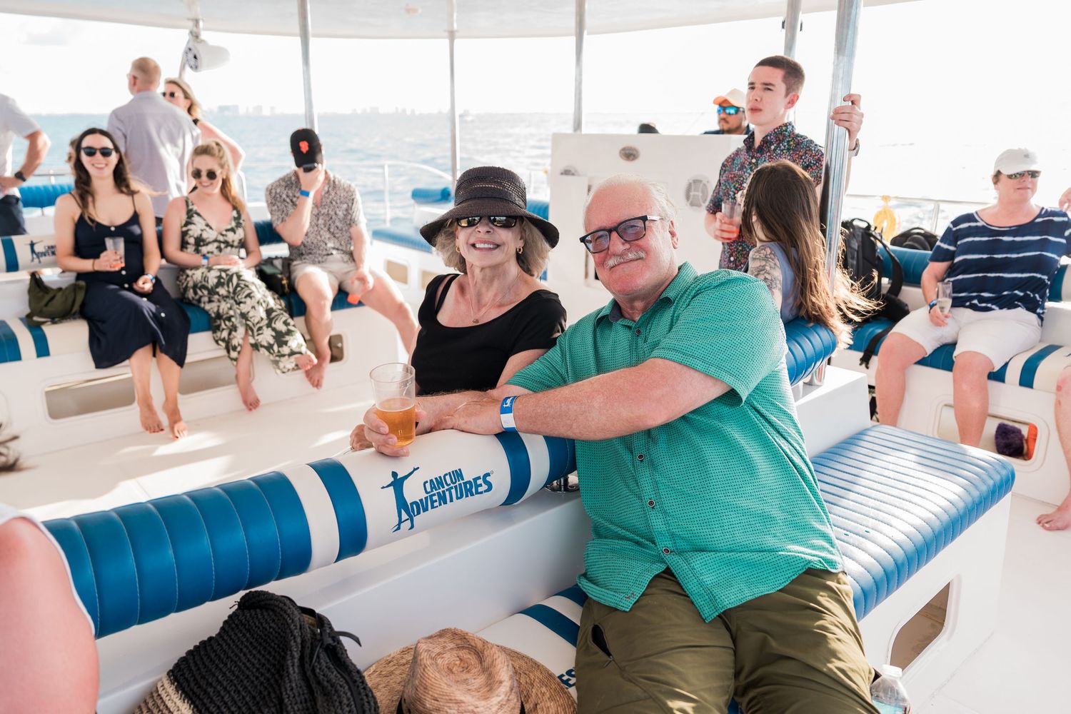 Smiling couple enjoying drinks on a scenic boat tour with other passengers on a sunny day.