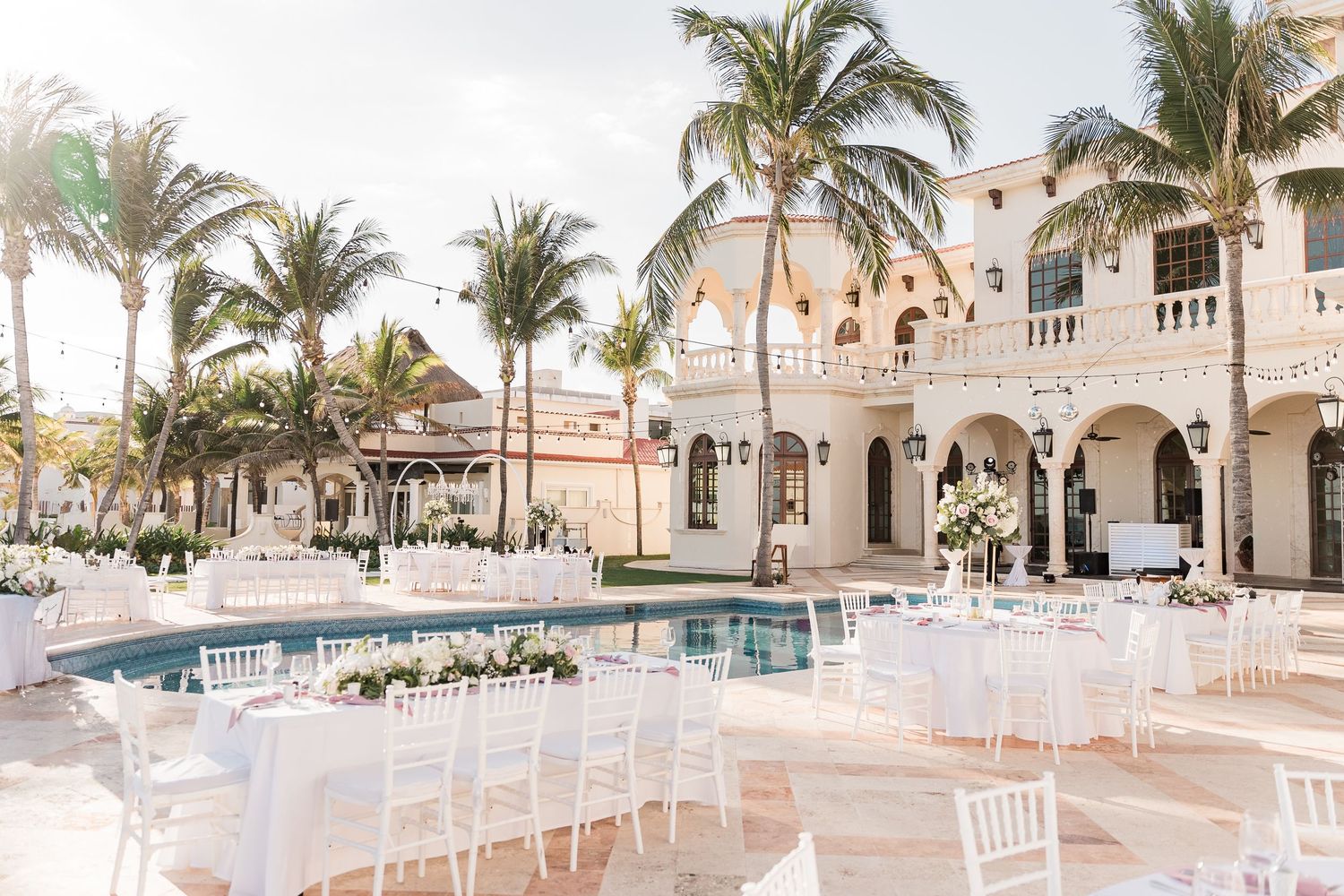 Elegant outdoor wedding reception with white chairs and tables beside a pool at a luxury villa.