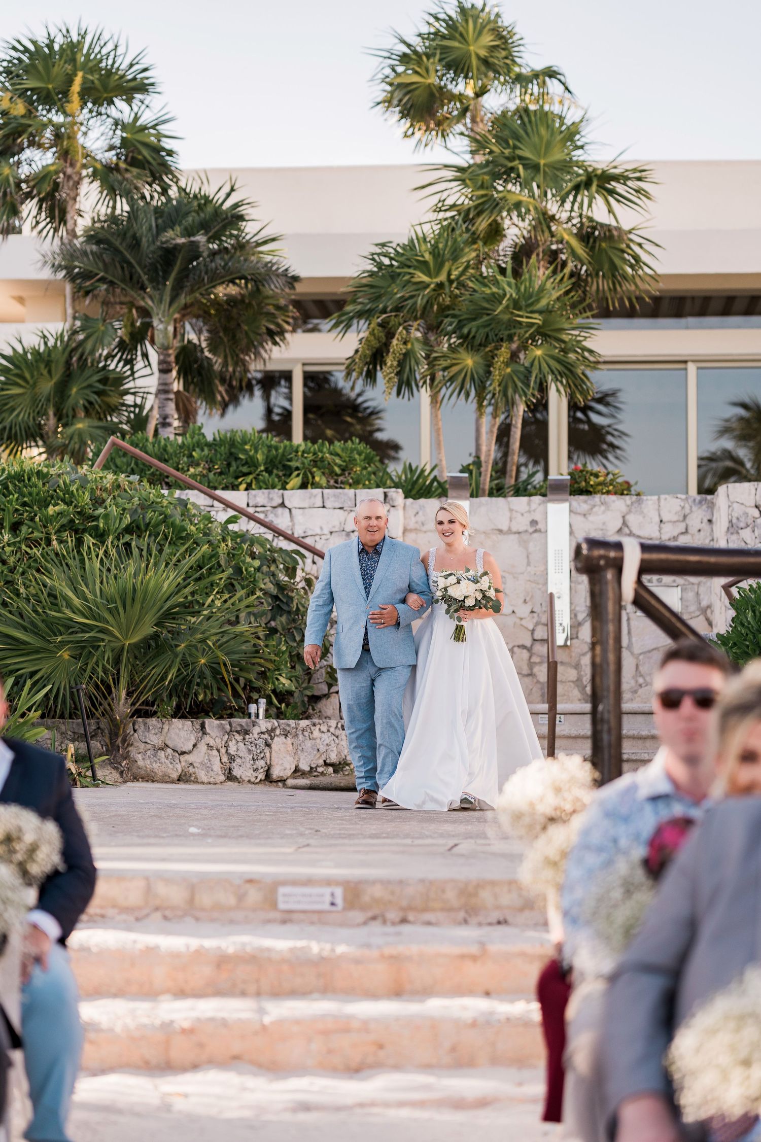 Bride in white gown walks down outdoor aisle with dad at Hard Rock Riviera Maya wedding