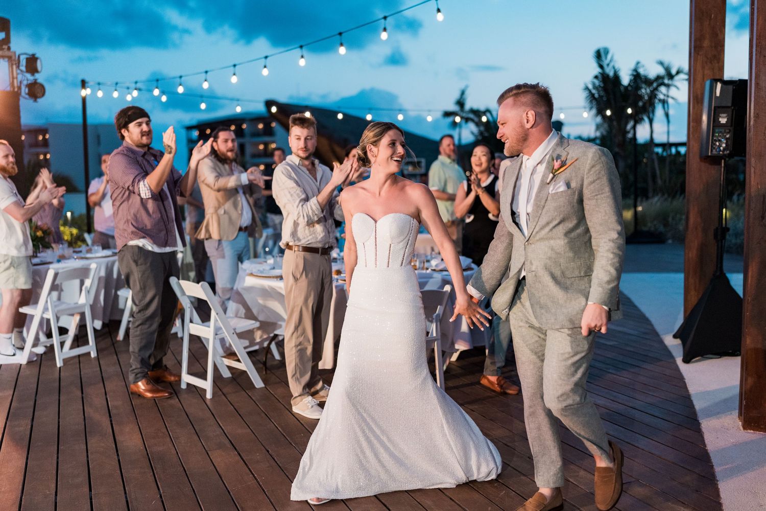 Bride and groom celebrate their first dance on an outdoor deck at a tropical beach wedding reception at dusk.