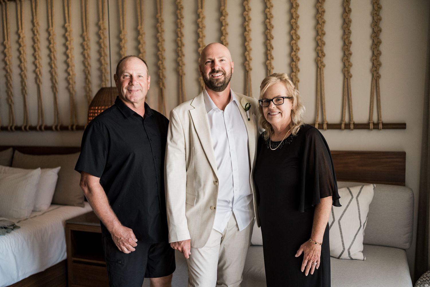 Three adults smiling together in an elegantly decorated room with macrame wall decor and neutral tones.