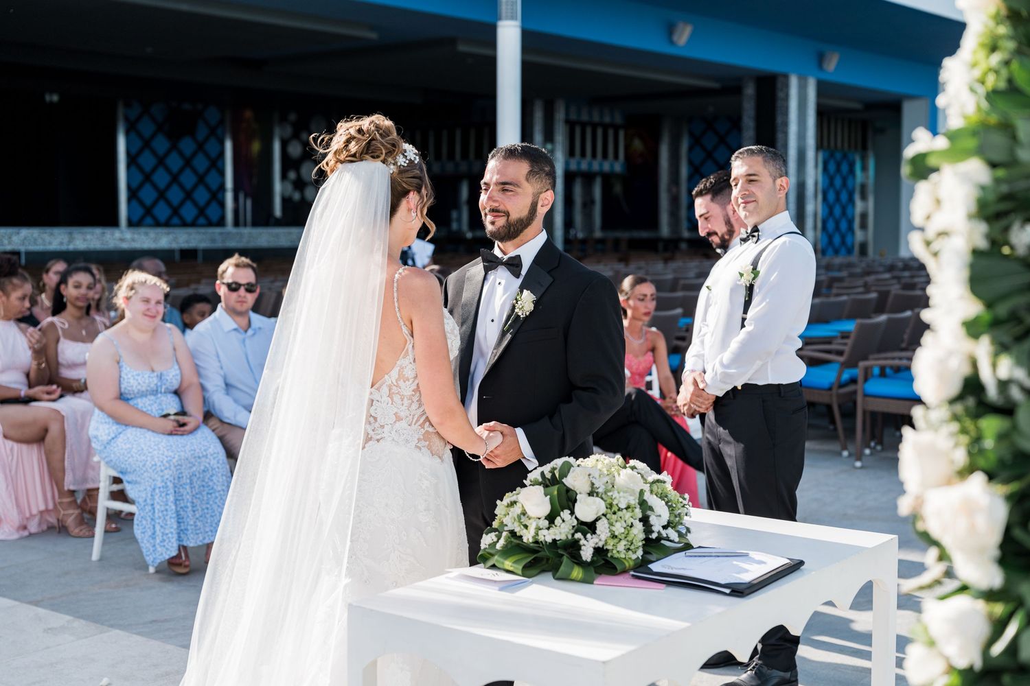 Bride and groom holding hands at decorated altar during intimate outdoor wedding ceremony with guests seated.