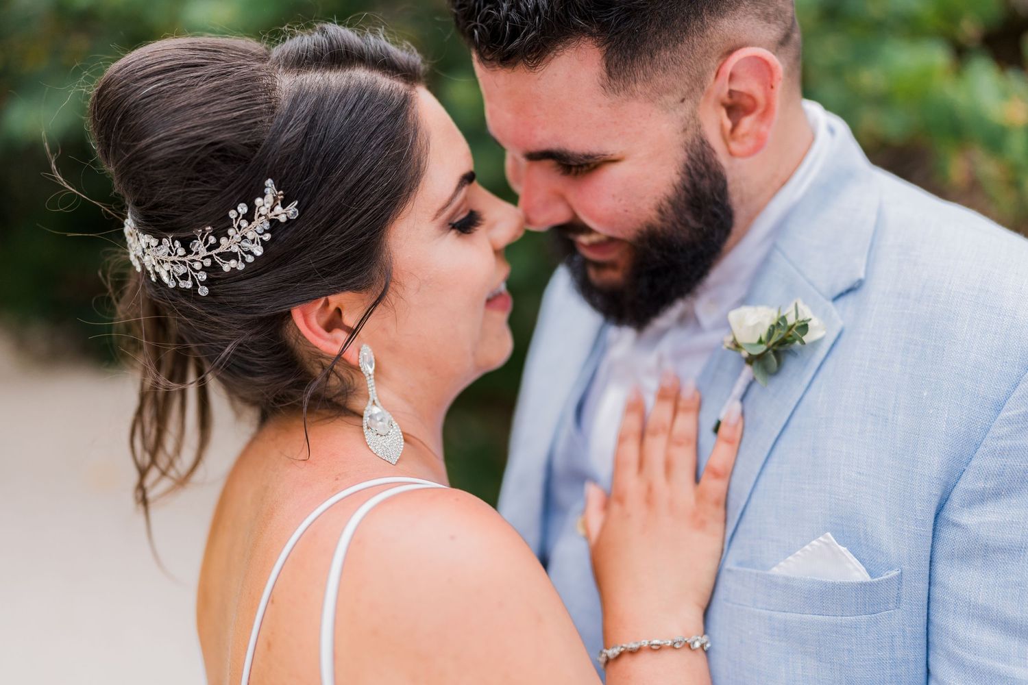 Bride and bearded groom share an intimate moment, bride wearing floral hair accessory and drop earrings.