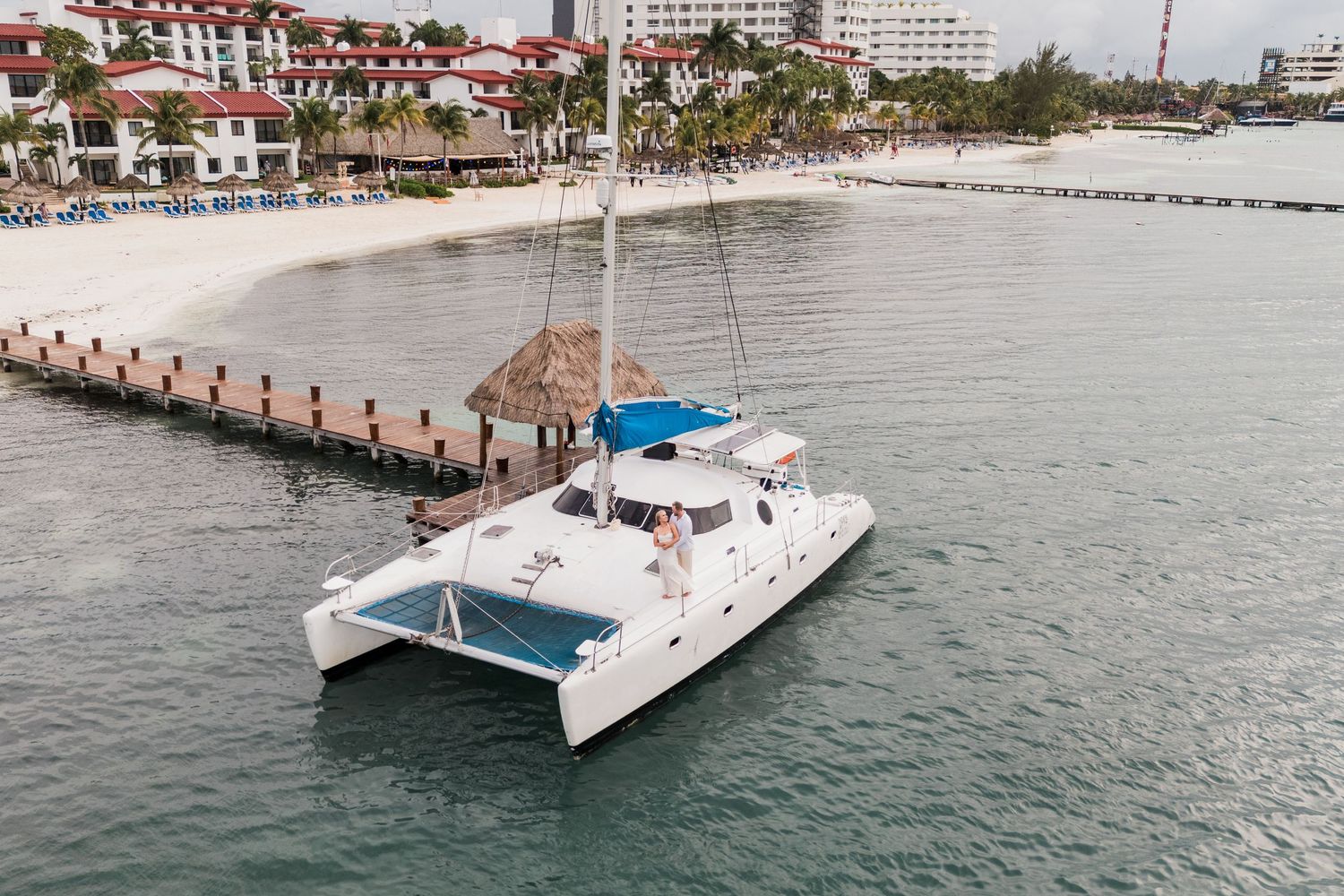 CANCÚN ENGAGEMENT PHOTOSHOOT - Drone Picture of White catamaran sailboat anchored near a tropical beach pier.