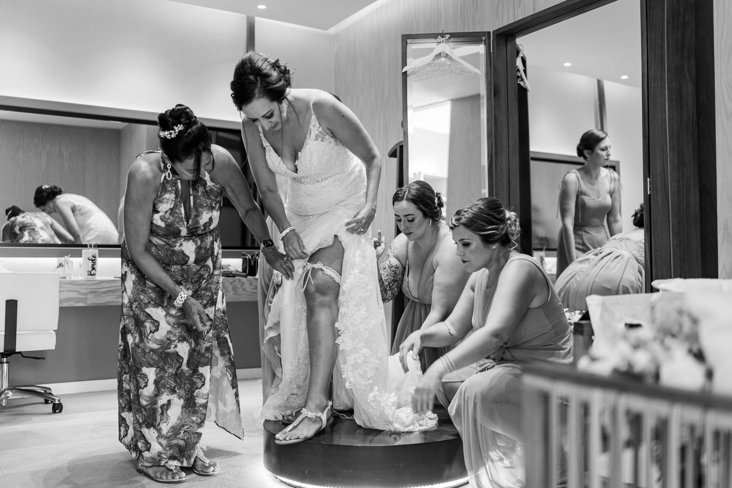 Bridesmaids help bride into wedding dress in bridal suite in black and white photo.