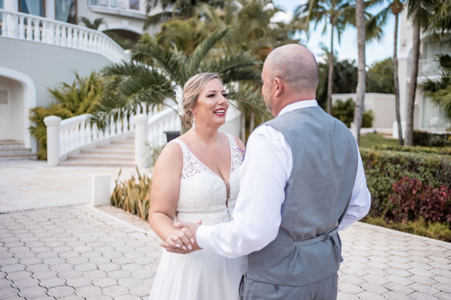 Bride and groom laugh together holding hands outside elegant white resort with palm trees.