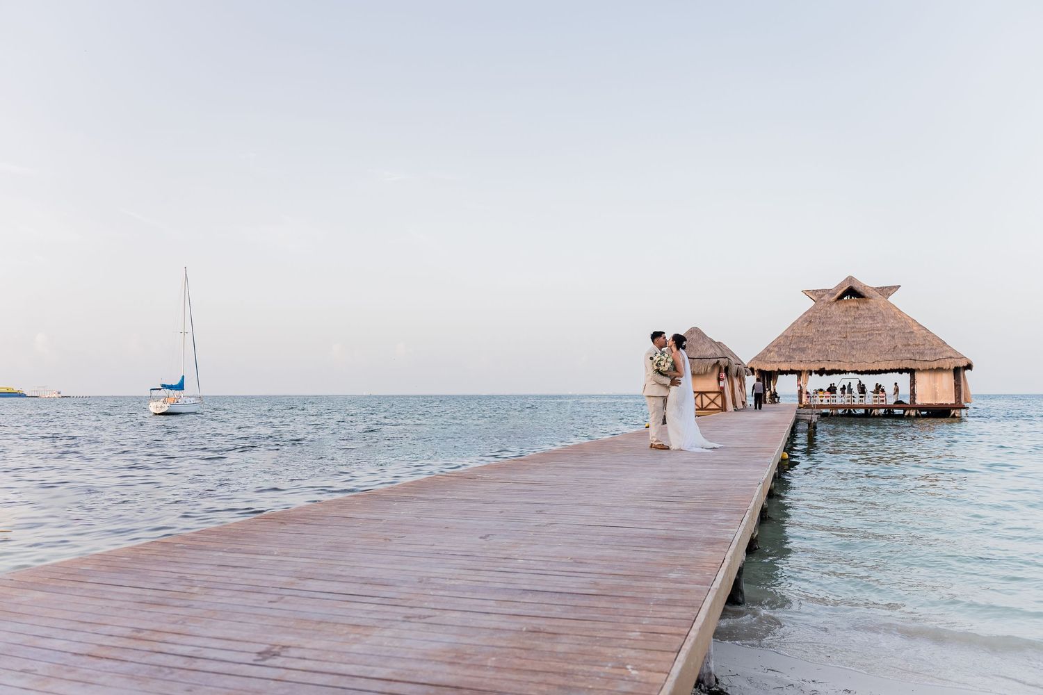 Newlyweds share romantic moment on wooden pier over turquoise Caribbean waters at sunset.