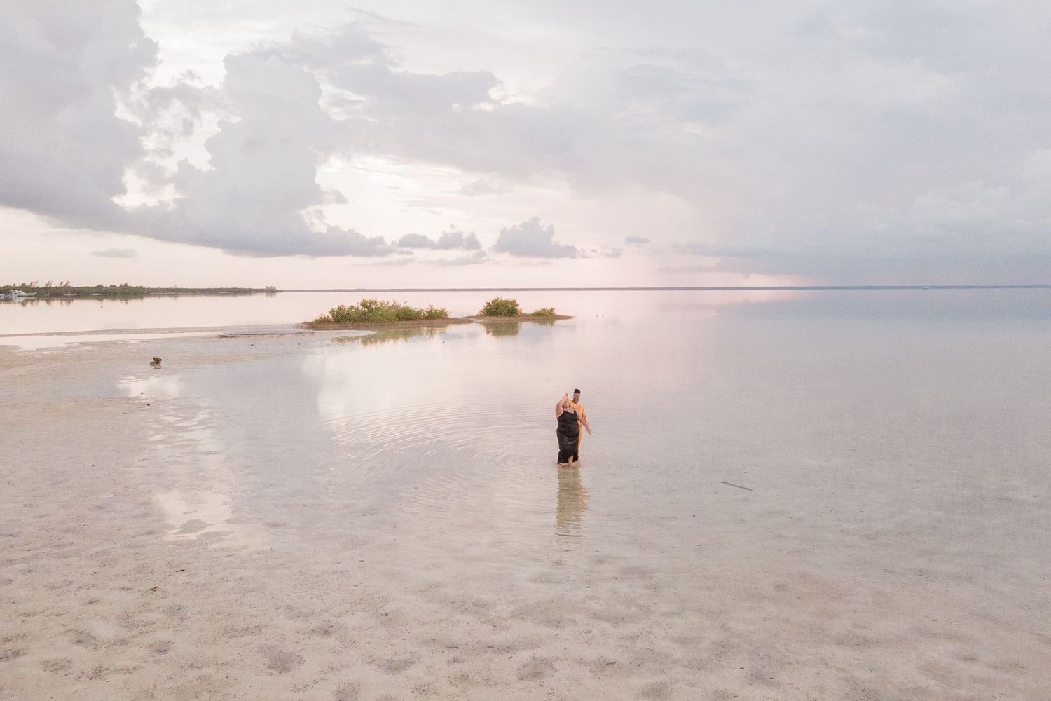 Woman standing alone in shallow water on a vast tranquil beach at dusk.