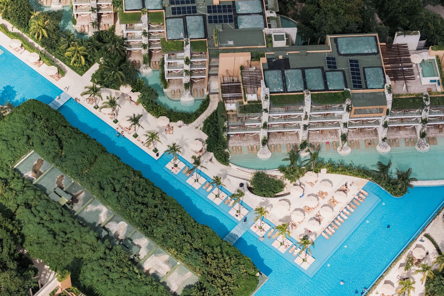 Xcaret Arte Wedding - Aerial view of a luxury resort with turquoise pools, sun loungers, and lush tropical greenery.