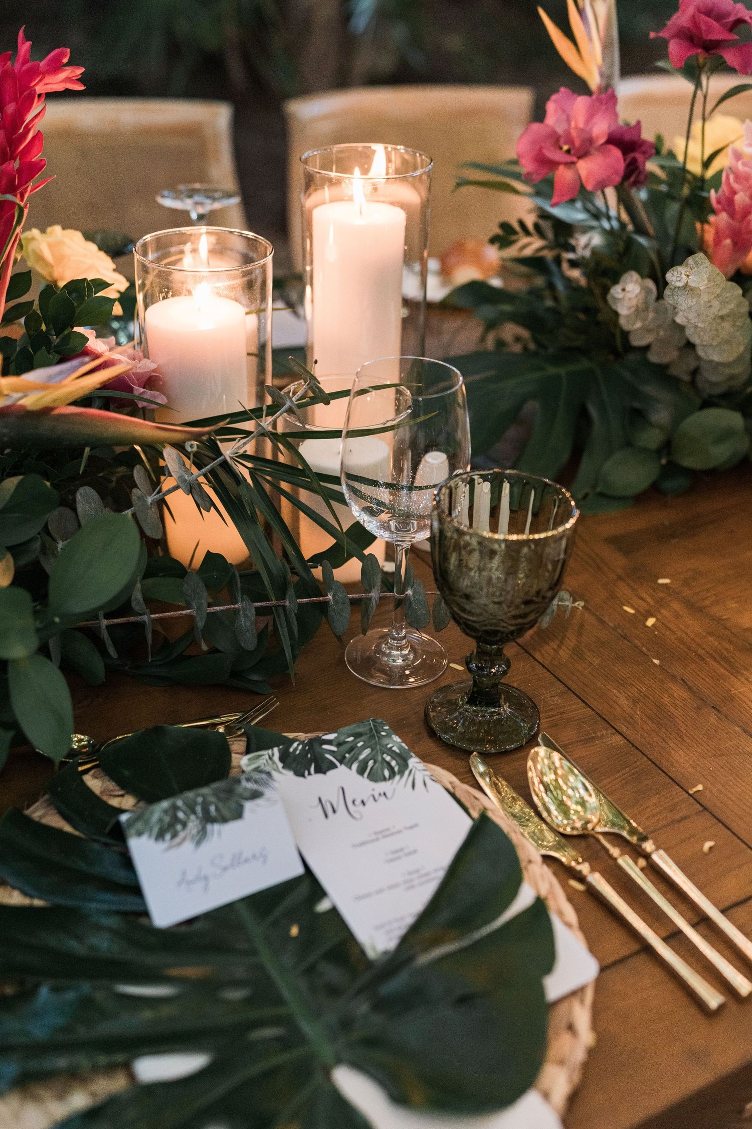Secrets Akumal Wedding - Tropical wedding table setting with candles, monstera leaves, gold cutlery, and vibrant floral centerpiece.