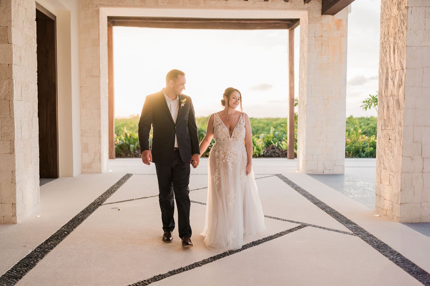 Bride and groom walk hand in hand through elegant outdoor venue with golden sunset backdrop on their wedding day at Puerto Vallarta