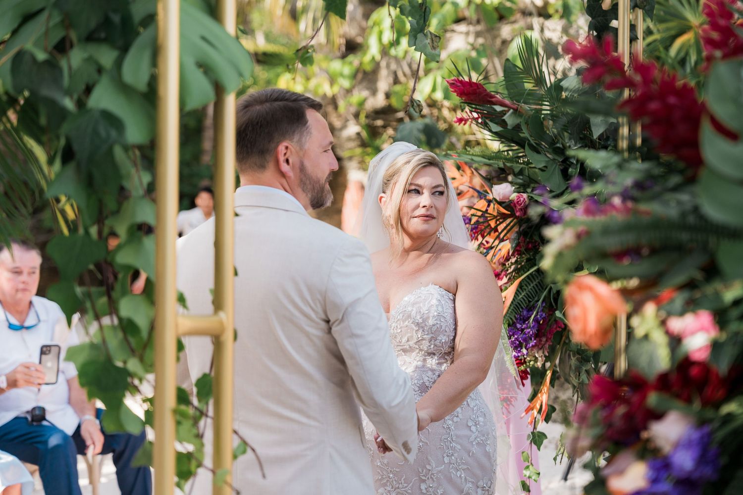 Bride and groom exchange vows at outdoor wedding ceremony surrounded by vibrant floral arrangements.