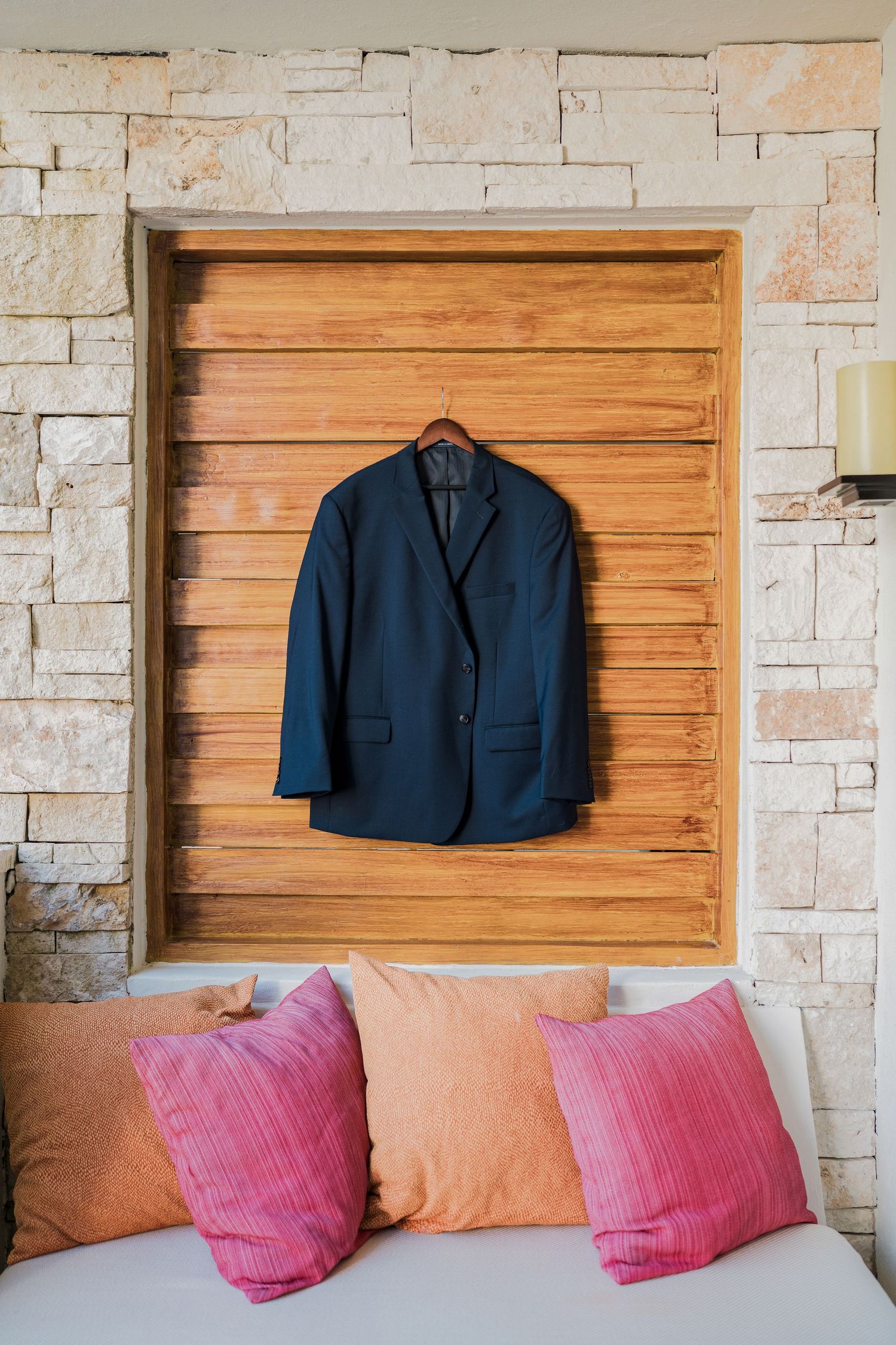 Secrets Akumal Wedding - Navy blue suit jacket hanging on a wooden panel wall above a couch with pink and orange pillows.