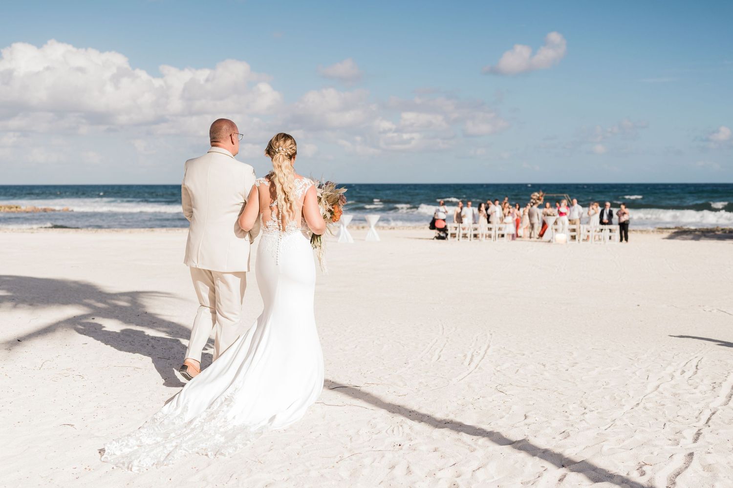 Bride and groom walk toward wedding party gathered on a pristine white sand beach ceremony.