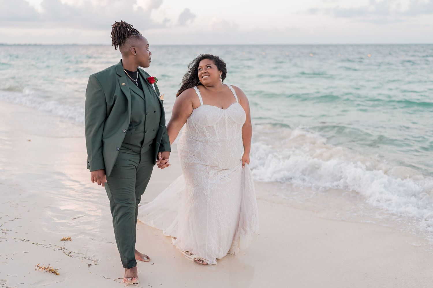Newlywed lesbian couple walks hand in hand along the shoreline of a beautiful turquoise Caribbean beach.
